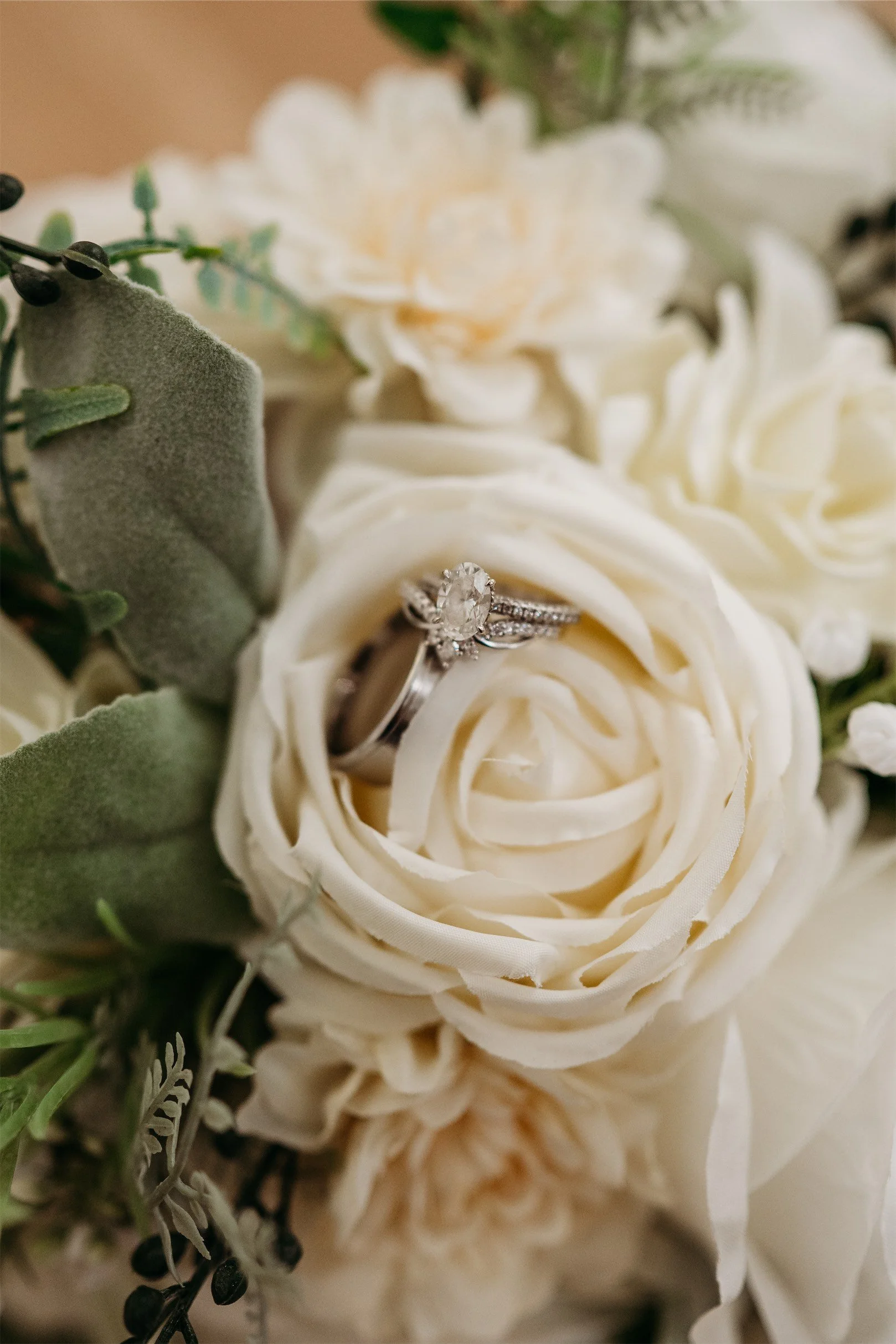 Diamond engagement ring and wedding band resting inside a cream rose in a bridal bouquet