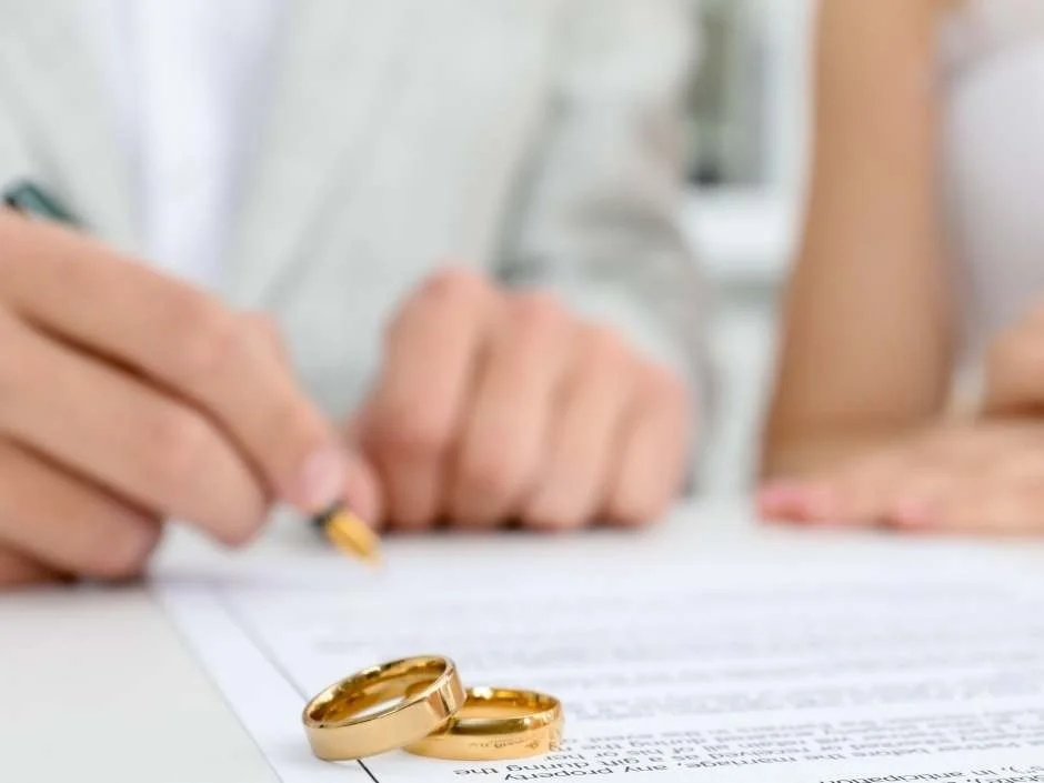 Person signing an Indiana marriage license with two gold wedding bands resting on the document