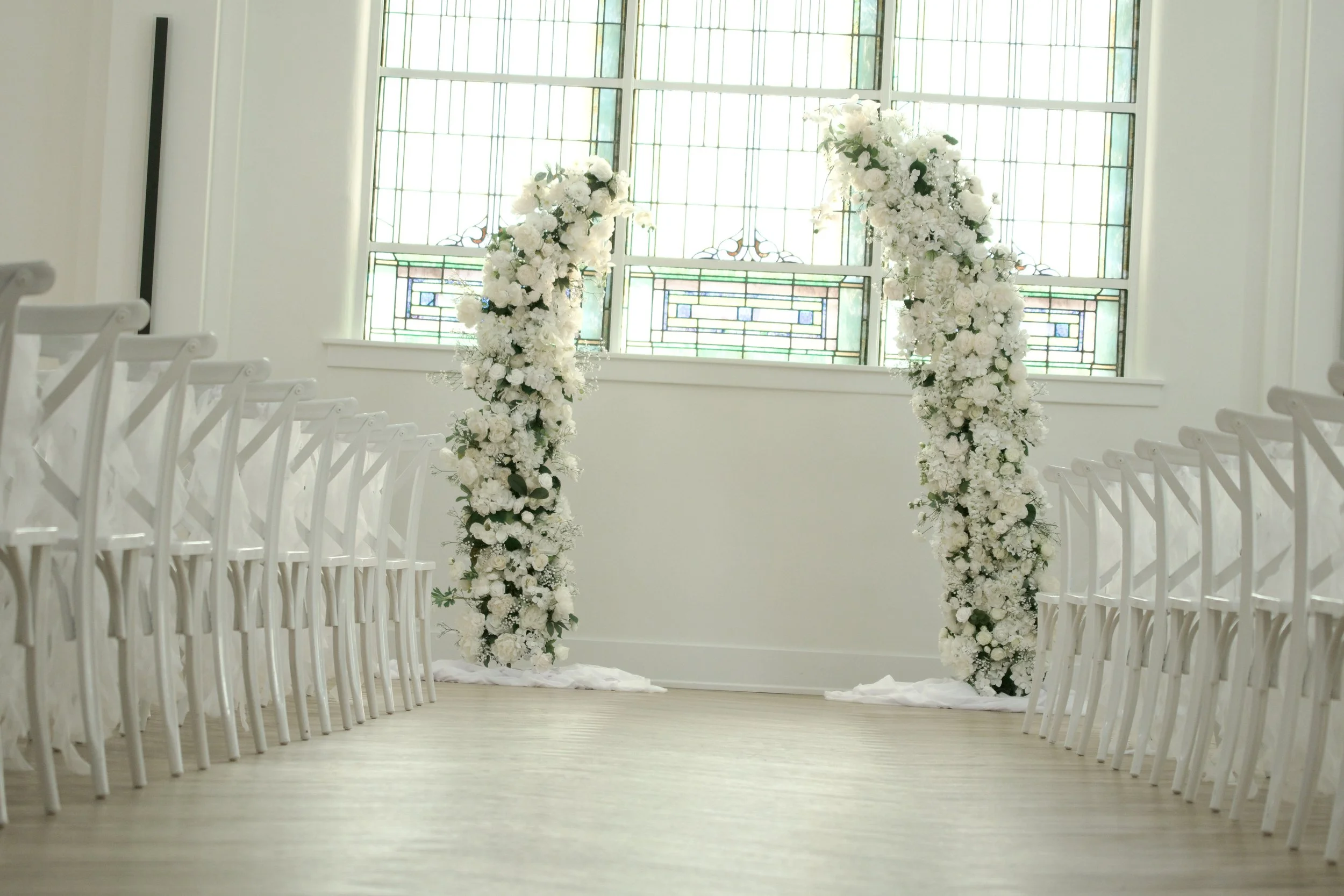 ceremony aisle view toward white floral columns and the stained glass altar window