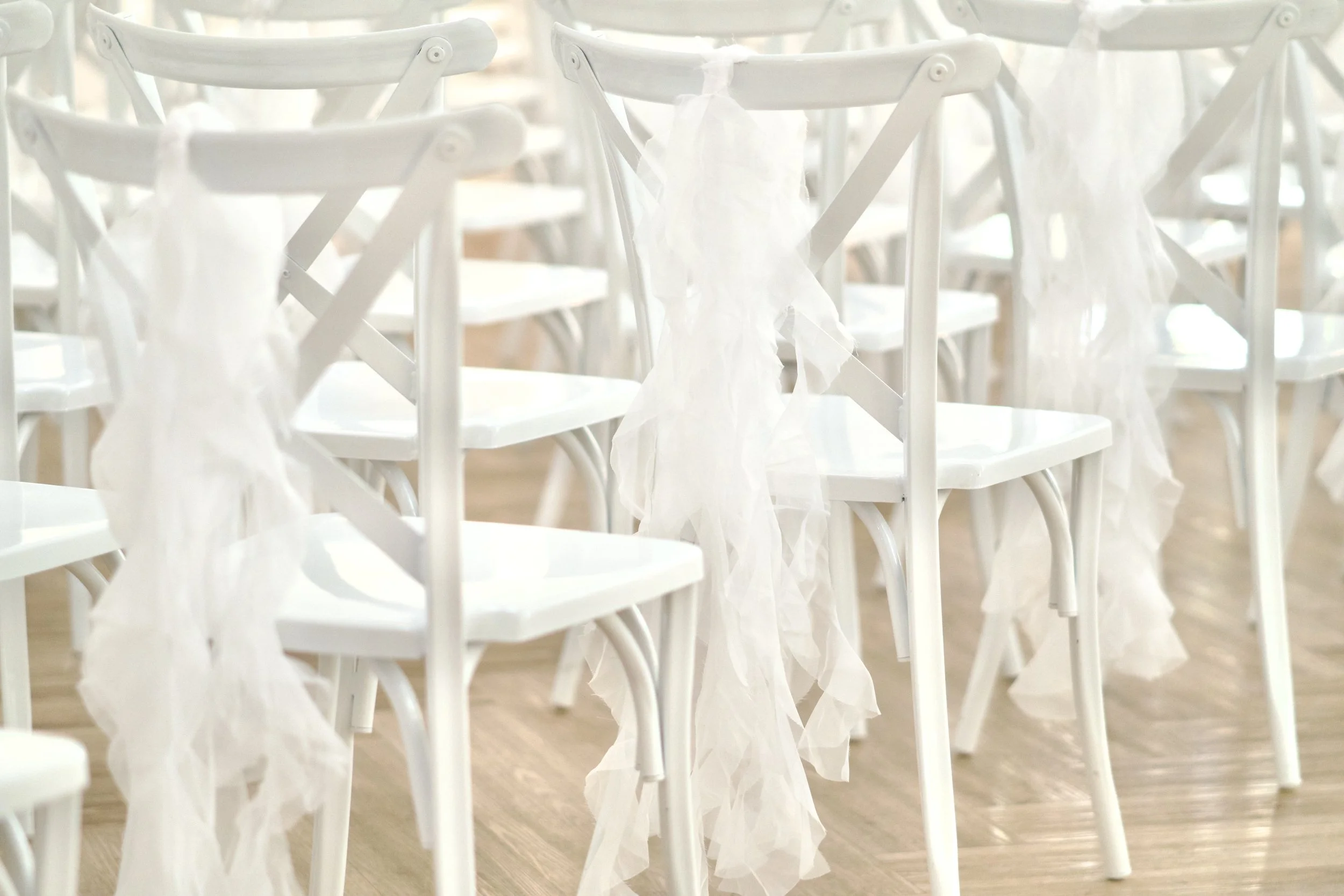 white cross back chairs draped with flowing sheer sashes at a Gatsby wedding ceremony