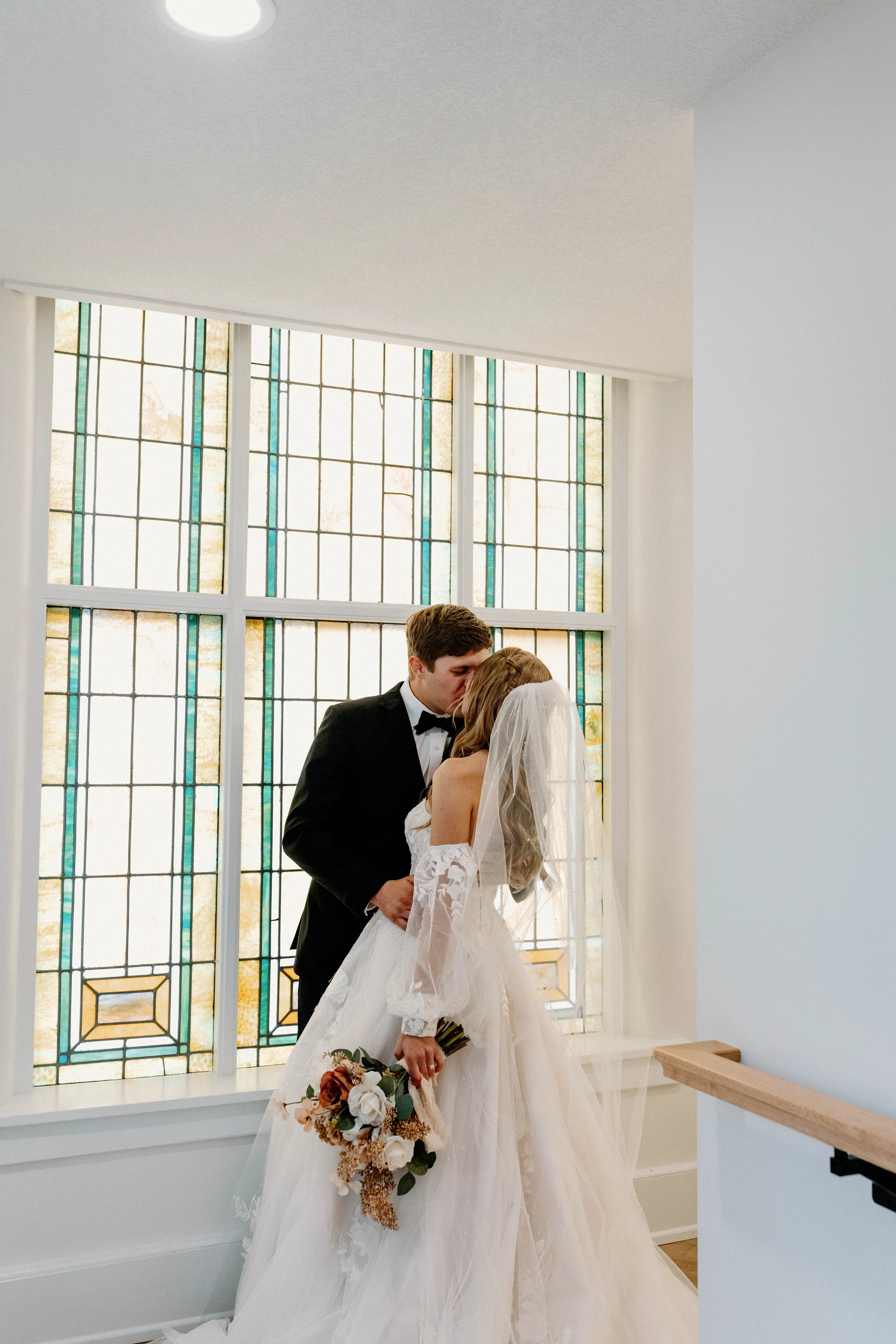 A bride and groom sharing a kiss in front of a stained glass window at their wedding.