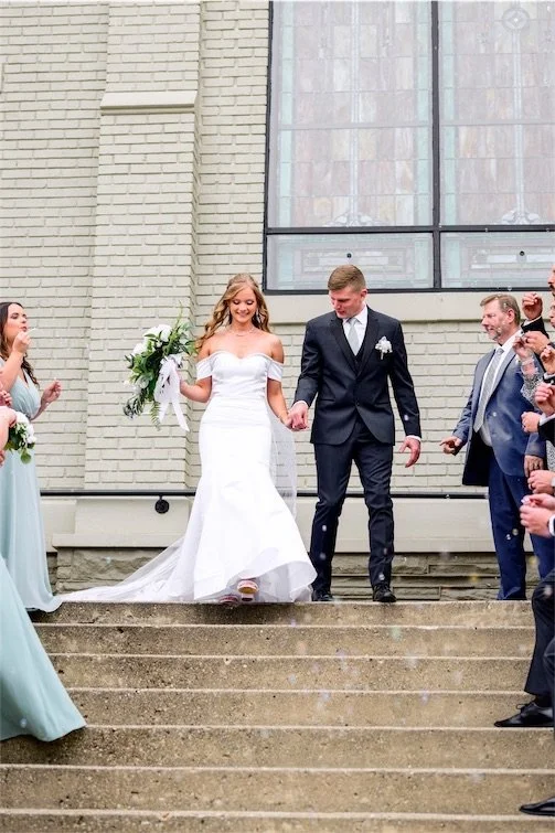 Bride and groom holding hands as they walk down cream brick church steps after their Indiana wedding ceremony