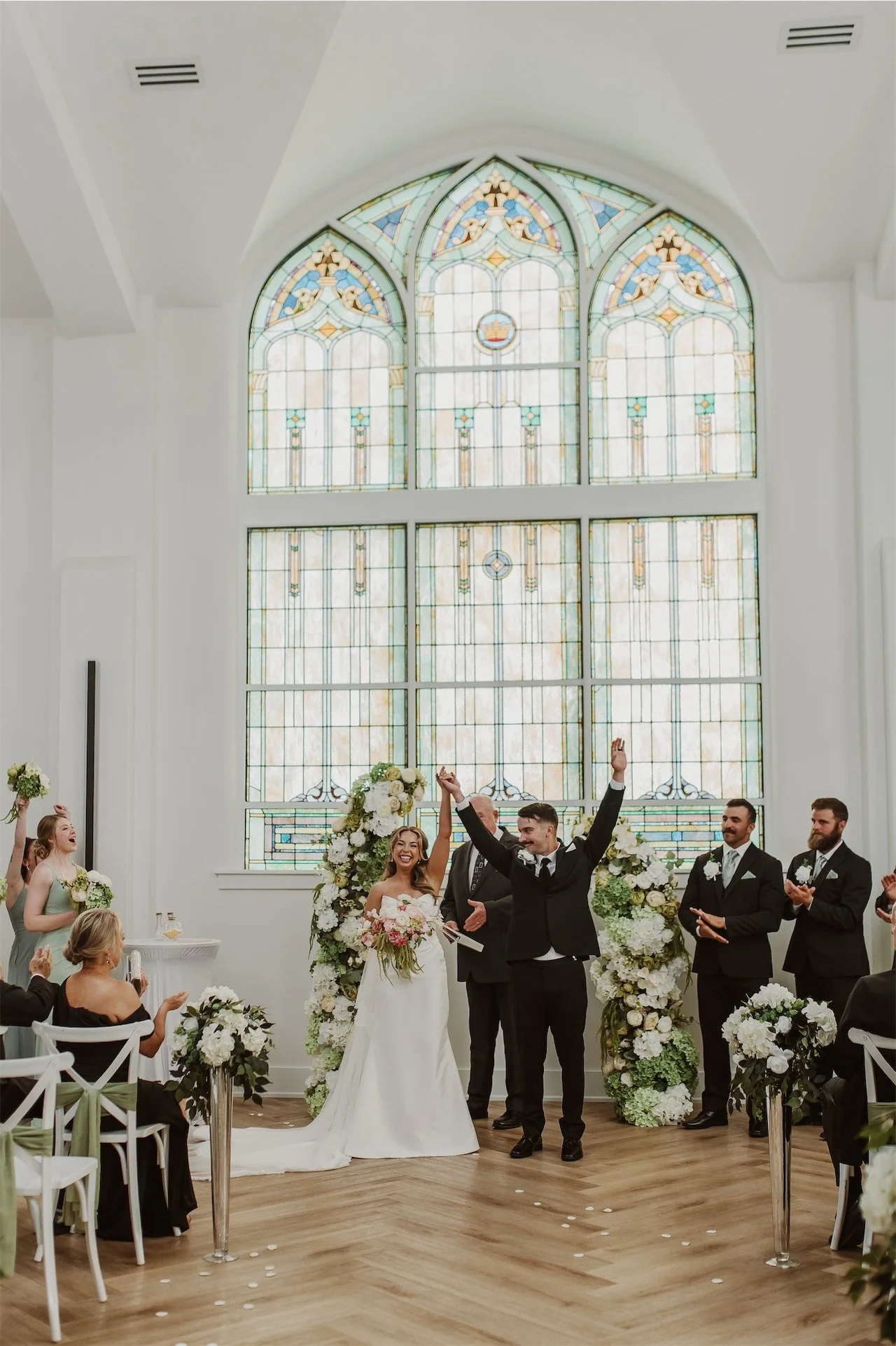 Newlyweds raising hands in celebration walking down aisle as guests applaud
