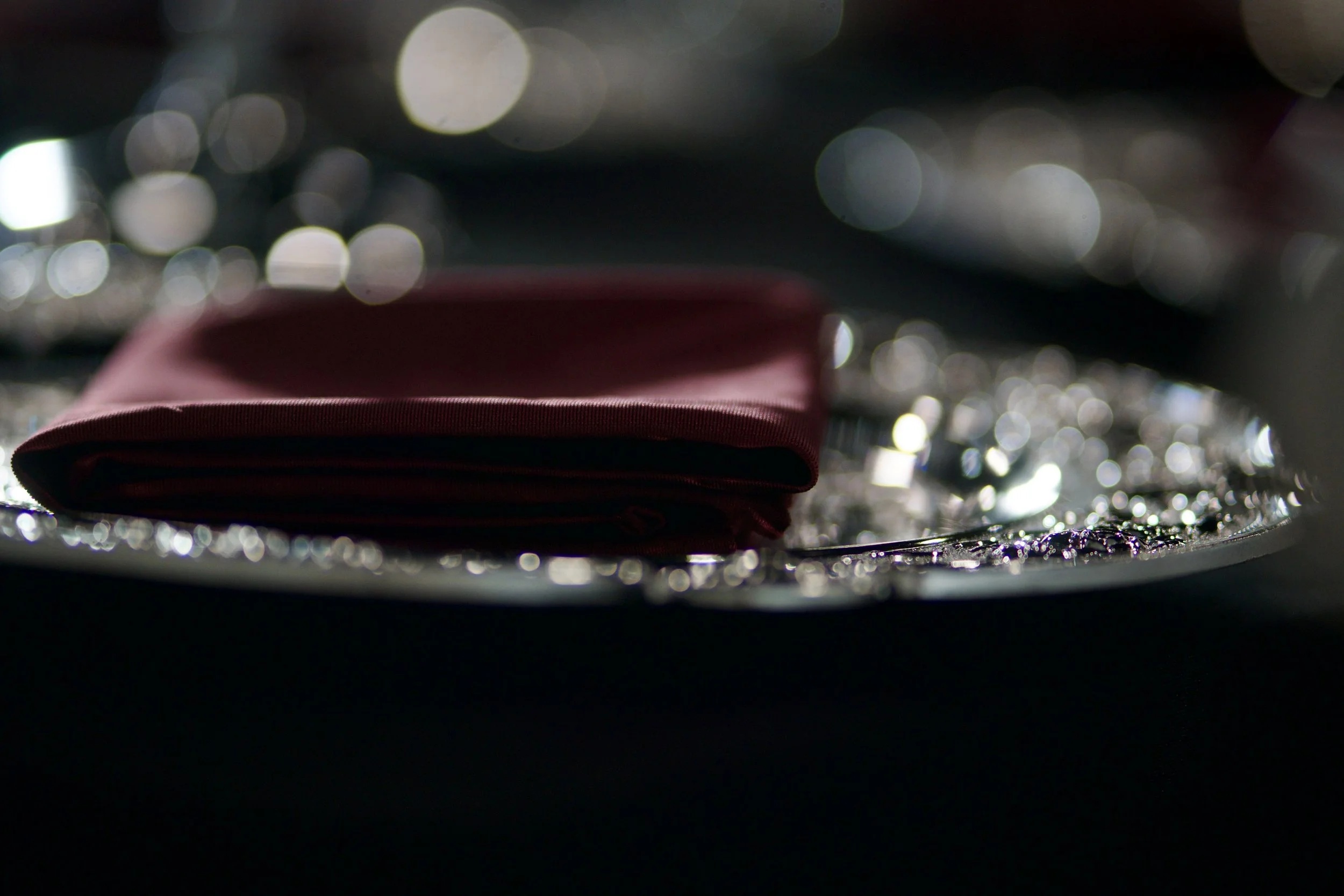 burgundy folded napkin resting on an ornate silver charger with candlelit bokeh