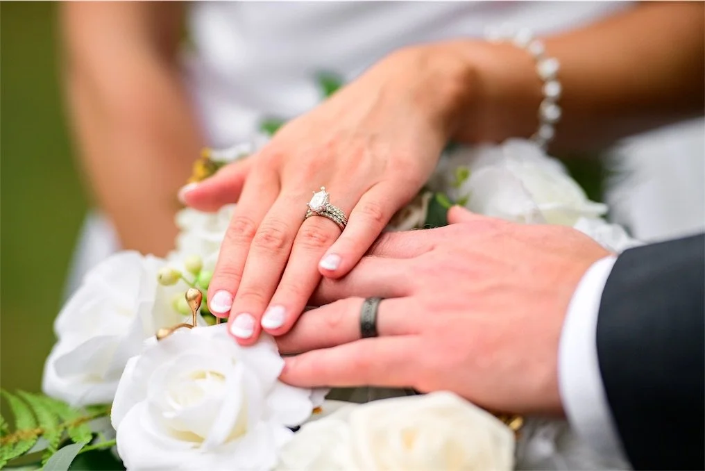 Close up of the couple's hands with wedding rings resting on a bouquet of white roses