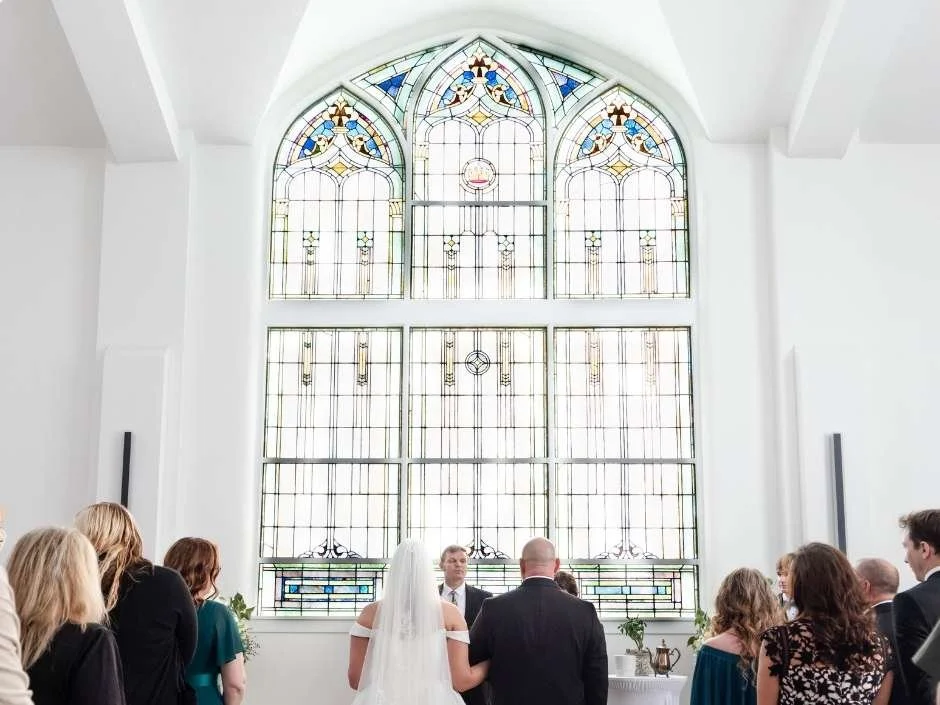 Bride and groom at the altar of Kaleidoscope Weddings with floor-to-ceiling stained glass windows in Pierceton Indiana