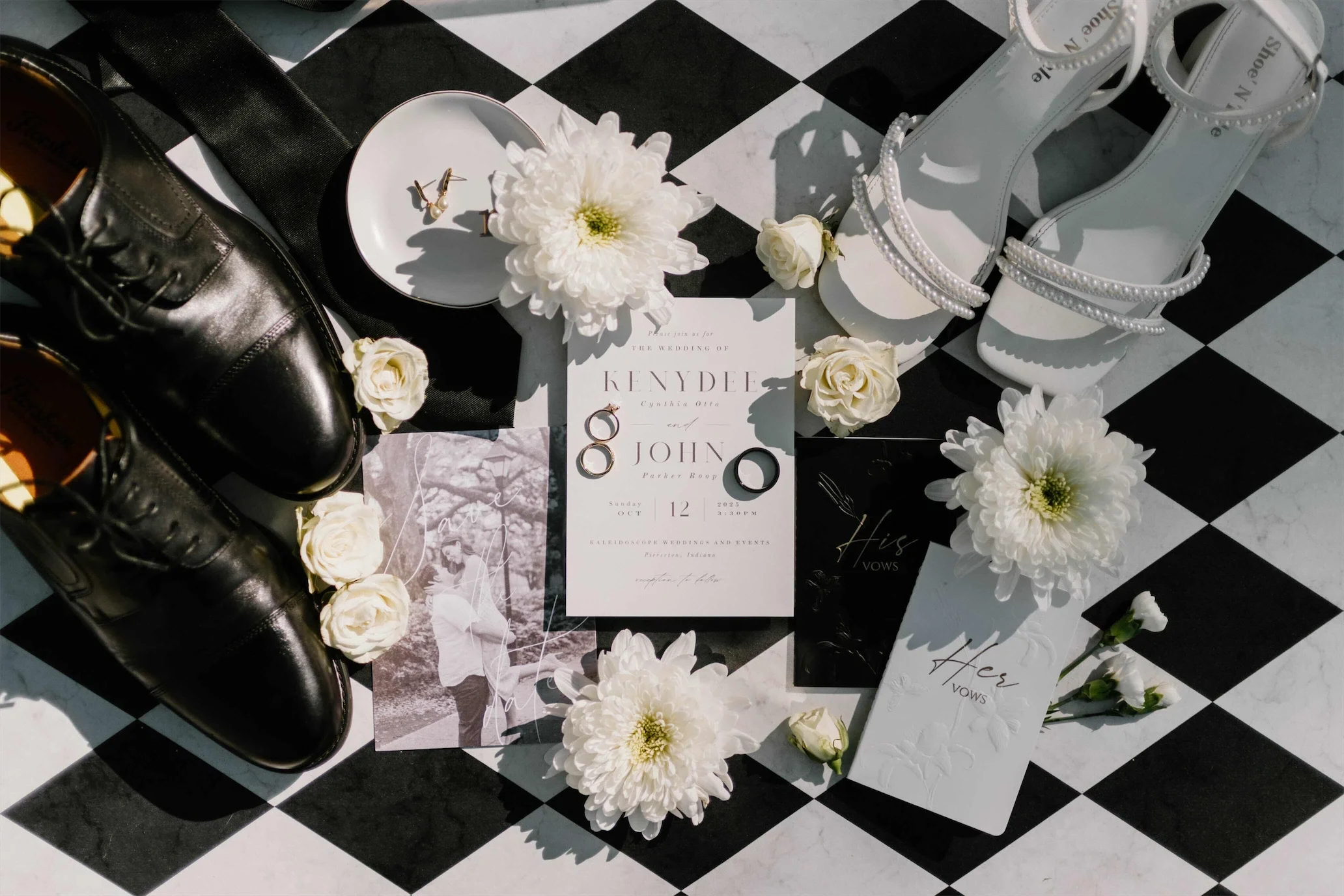 Checkered Chic wedding flat lay with invitation, rings, pearl heels, black oxfords, and white mums on checkered tile