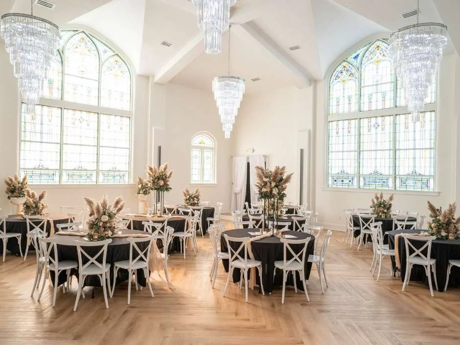 Kaleidoscope Weddings reception room set for a boho-themed seated dinner with crystal chandeliers and stained glass windows