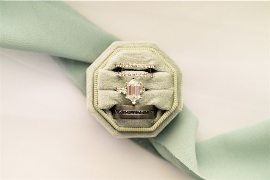 Engagement ring and wedding bands nestled in a sage green velvet ring box