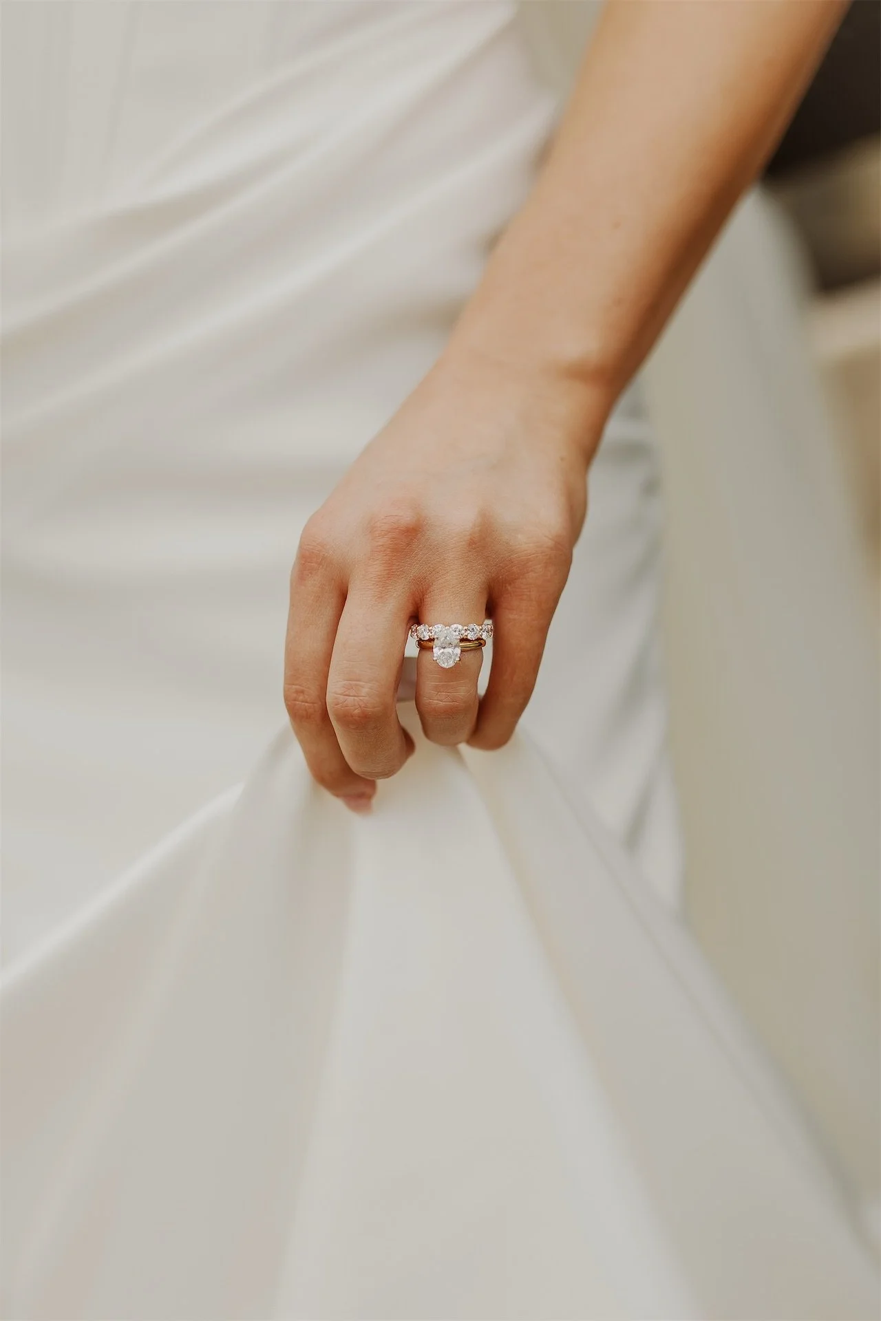 Close up of brides hand and wedding ring resting on satin gown