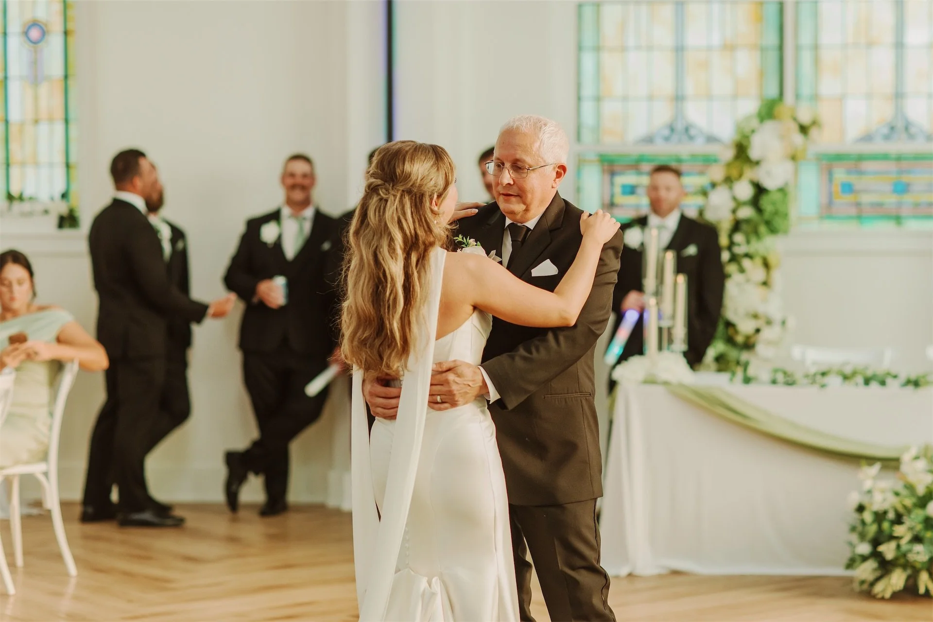 Bride dancing with her father during reception beneath stained glass windows