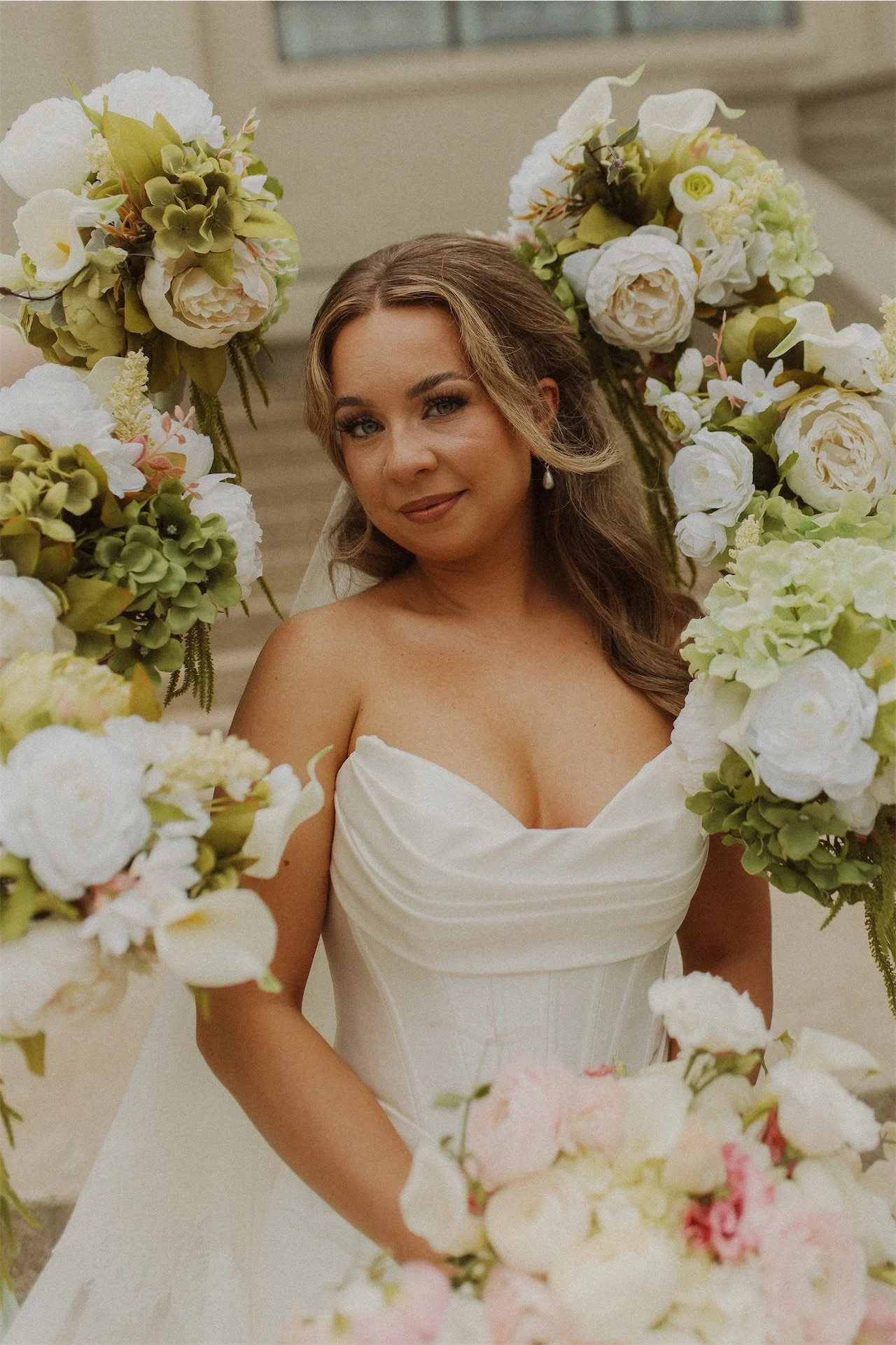 Bride framed by white and green floral arrangements smiling softly