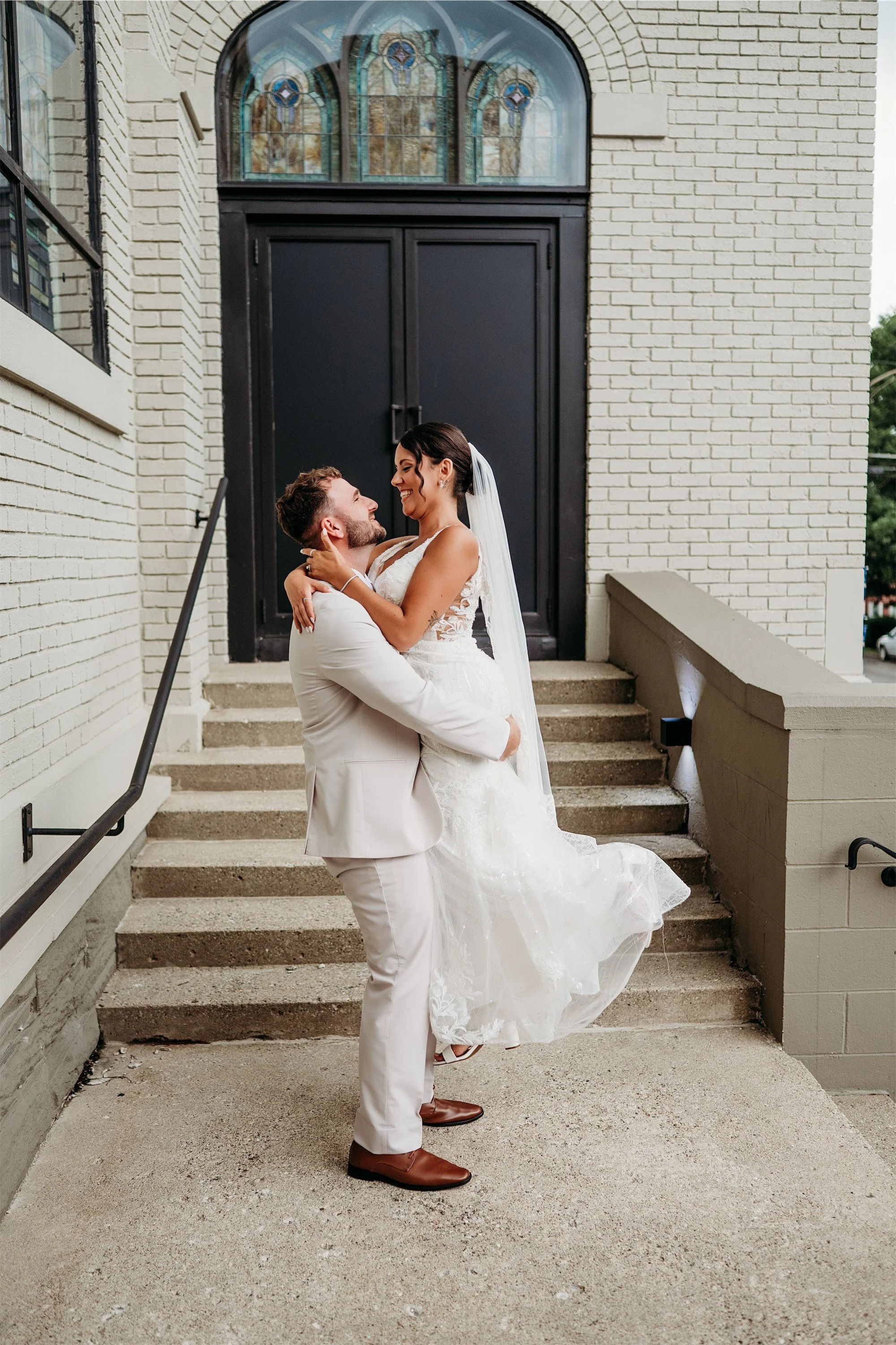 Groom lifting the bride in his arms on the front steps of the historic church venue