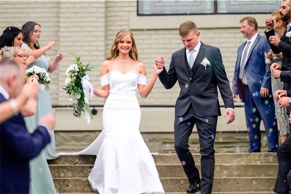 Newlyweds hold hands and walk down steps through cheering guests after the ceremony