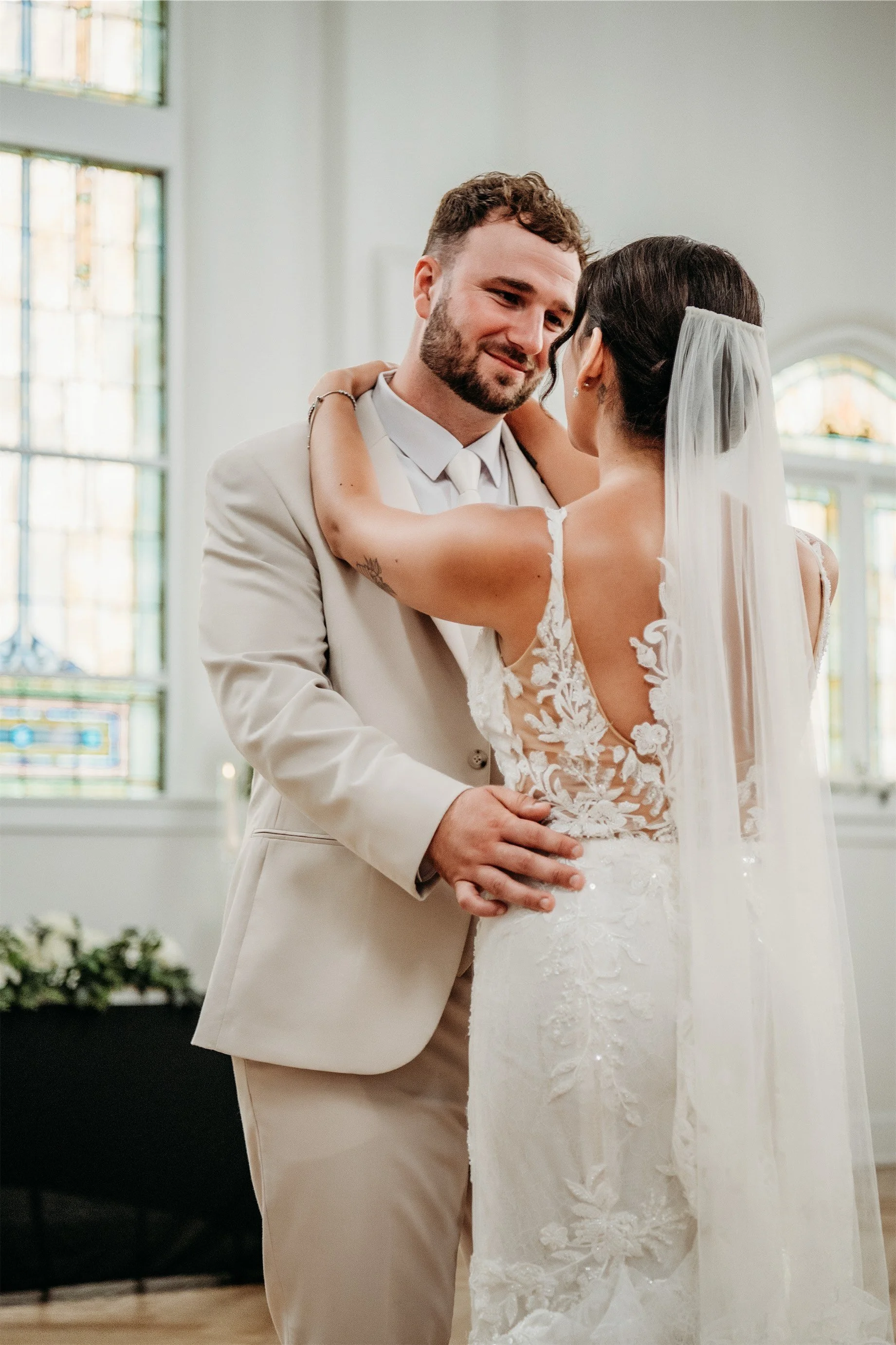 Groom smiling down at the bride during their first dance in front of tall stained glass windows