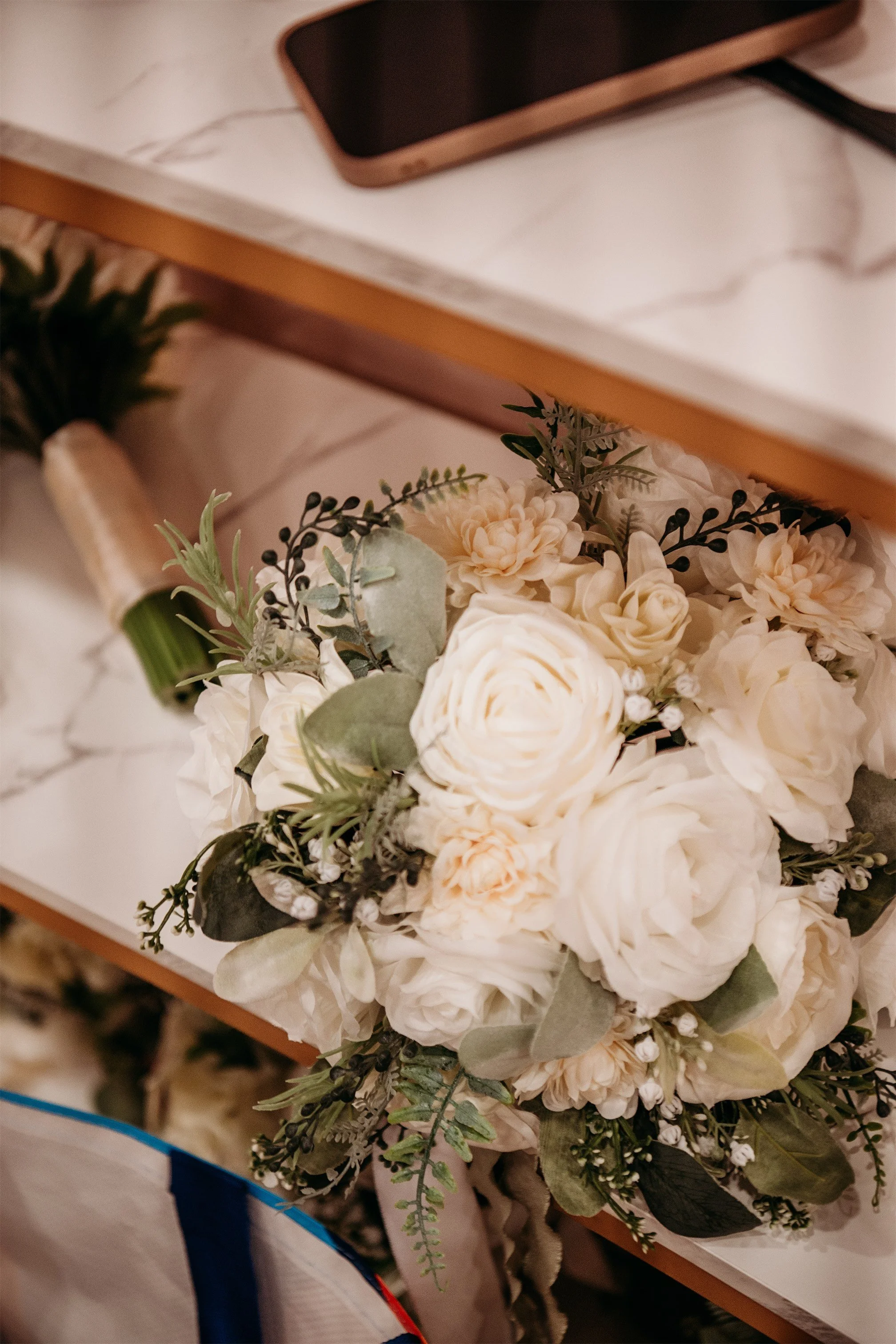 White rose and cream dahlia bridal bouquet with eucalyptus and baby's breath resting on a marble shelf
