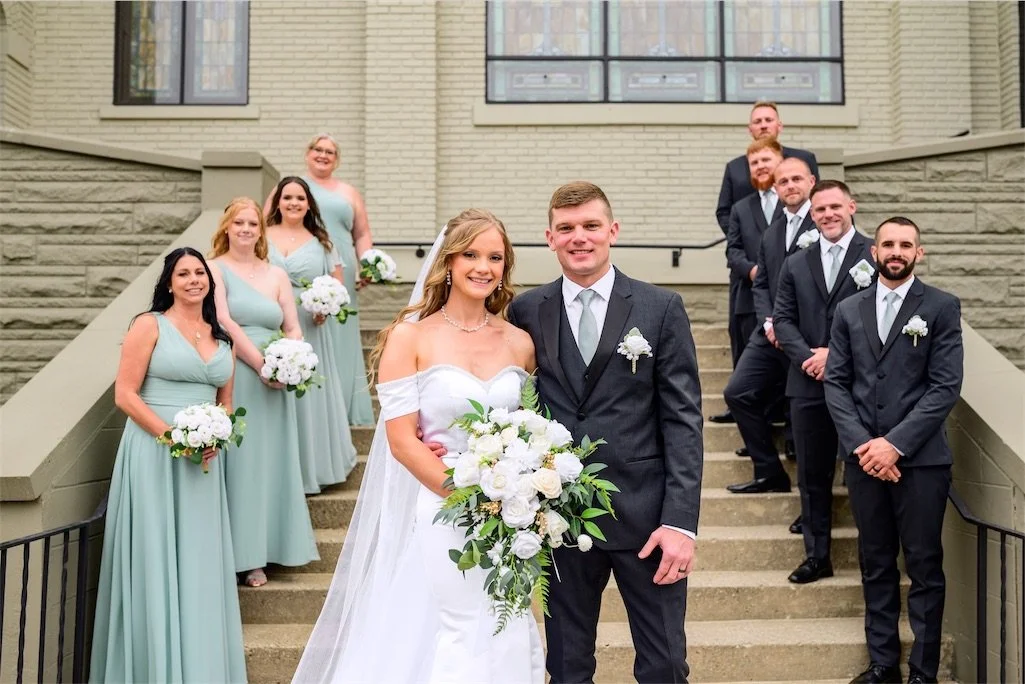 Bride and groom pose in front with bridesmaids and groomsmen lined up behind them on church steps