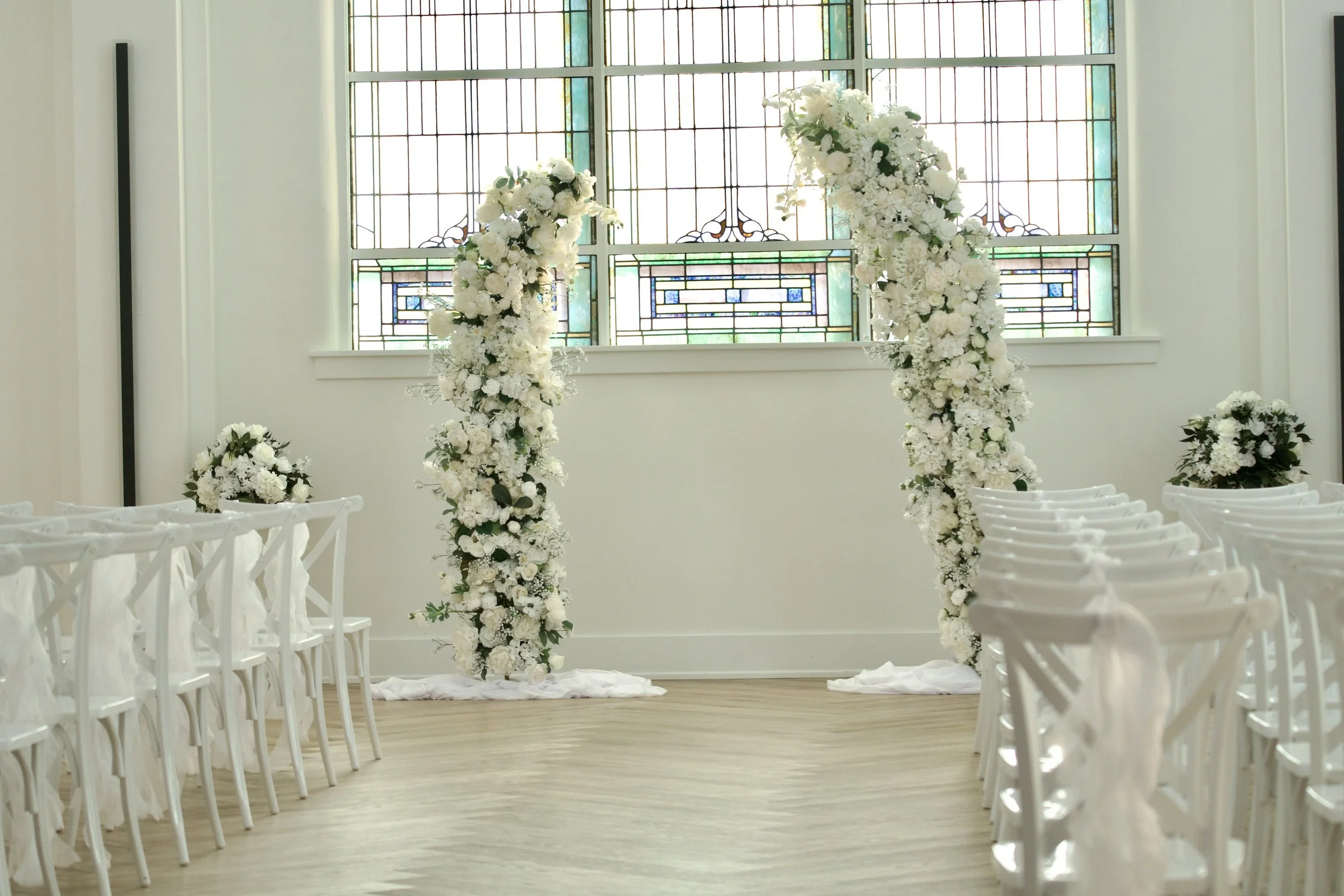 white rose and hydrangea arrangements flanking the historic stained glass altar wall
