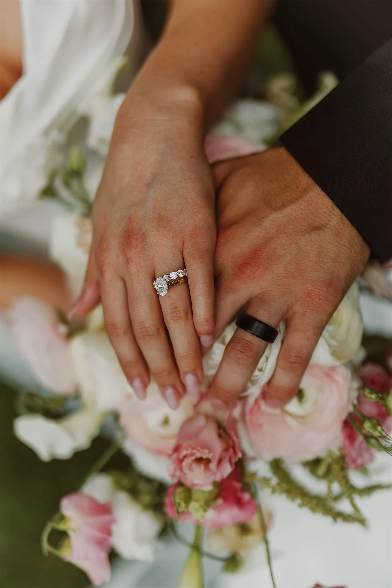 Bride and groom hands resting together showing wedding rings over bouquet