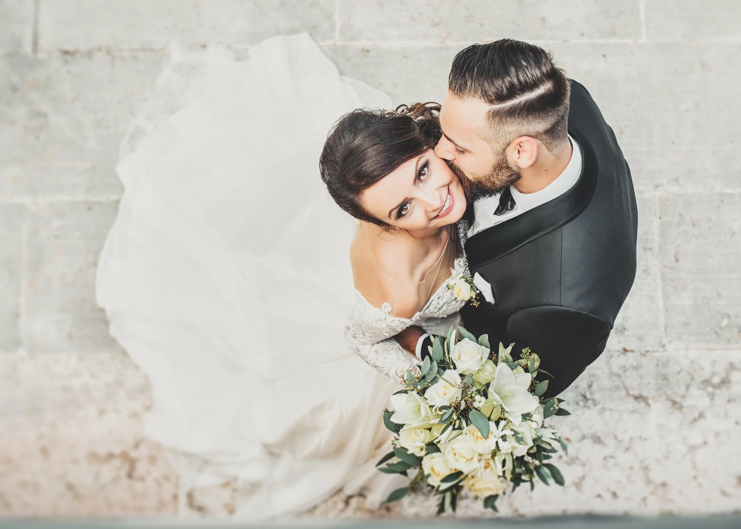 bride and groom embracing with groom kissing her cheek, holding white bouquet