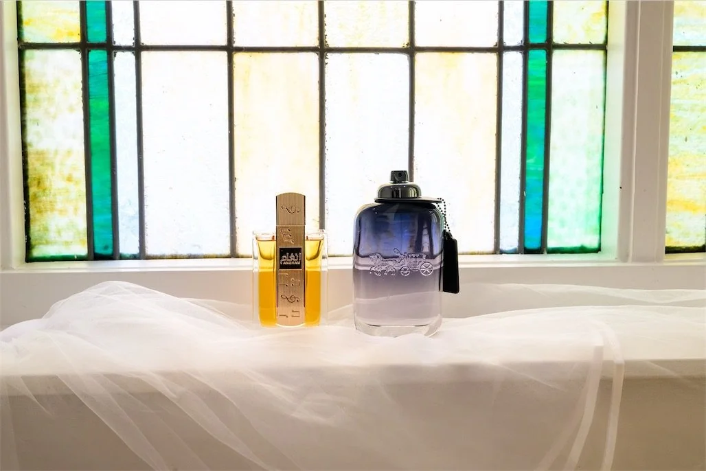 Two cologne bottles standing on a veil draped windowsill in front of stained glass