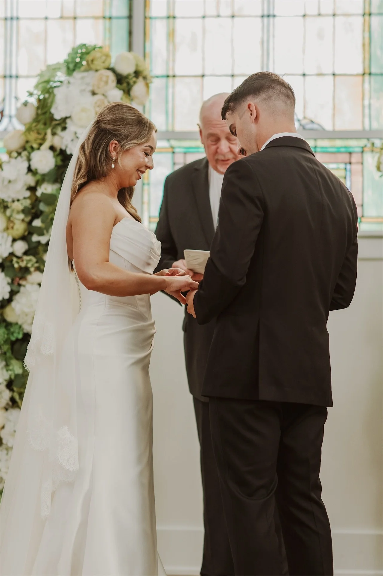 Bride and groom exchanging wedding rings with officiant at church ceremony