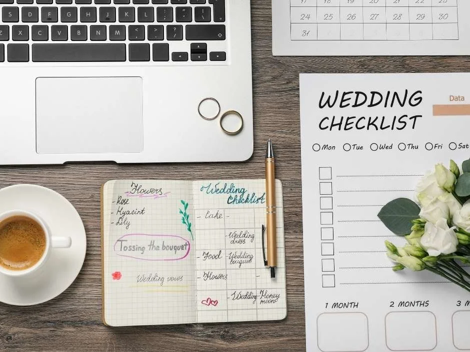 Open wedding checklist notebook and printed planning form on a wood desk with gold rings and flowers