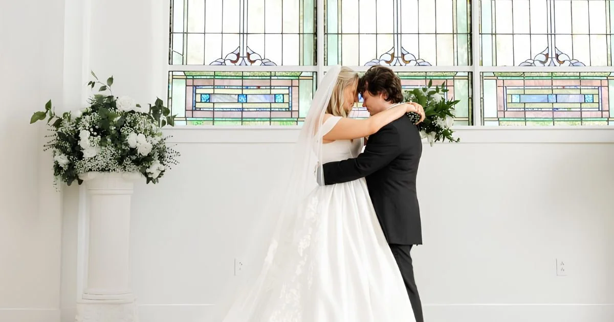bride and groom embracing beneath arched stained glass windows at their ceremony