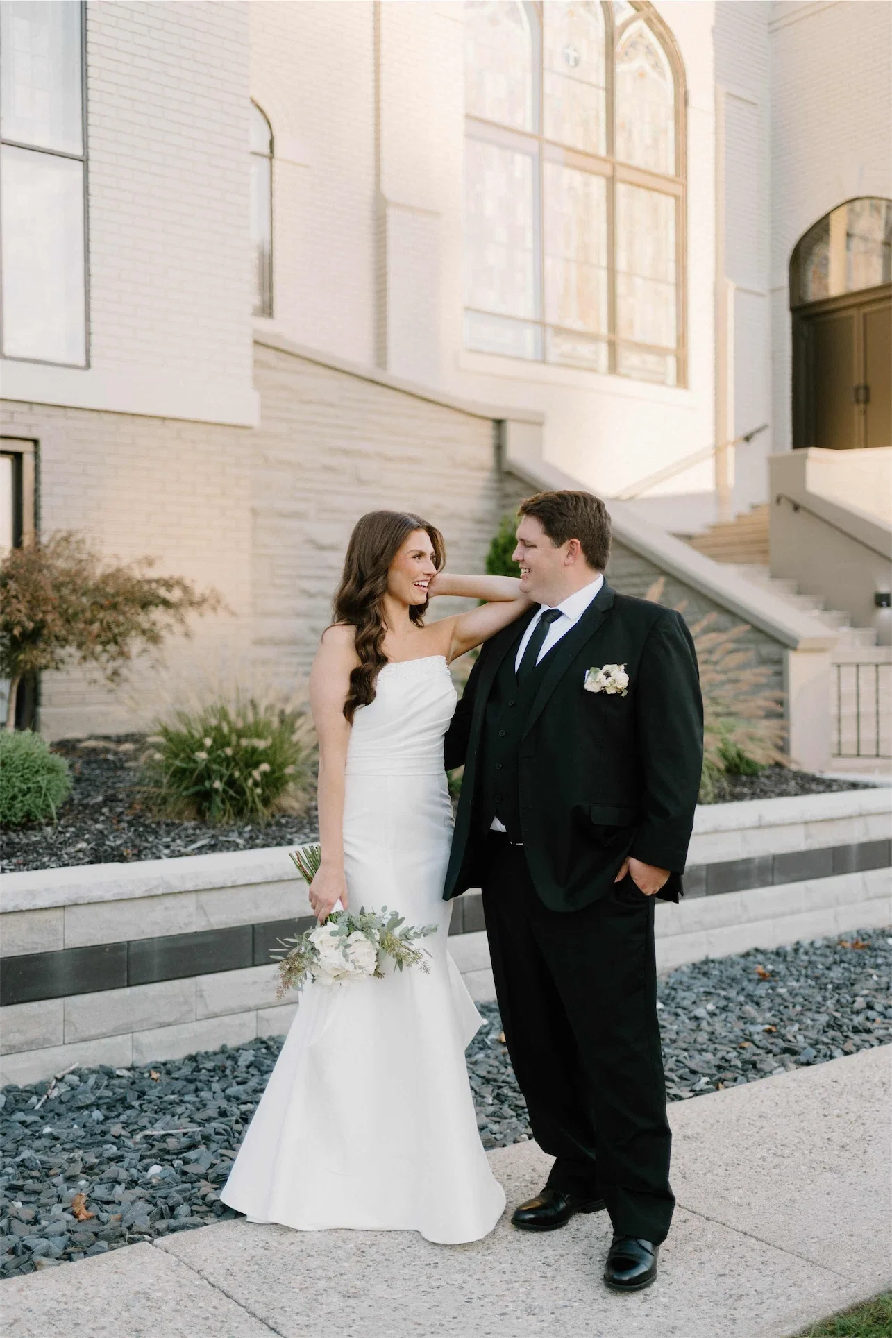 Bride and groom smiling at each other beside the chapel's exterior staircase