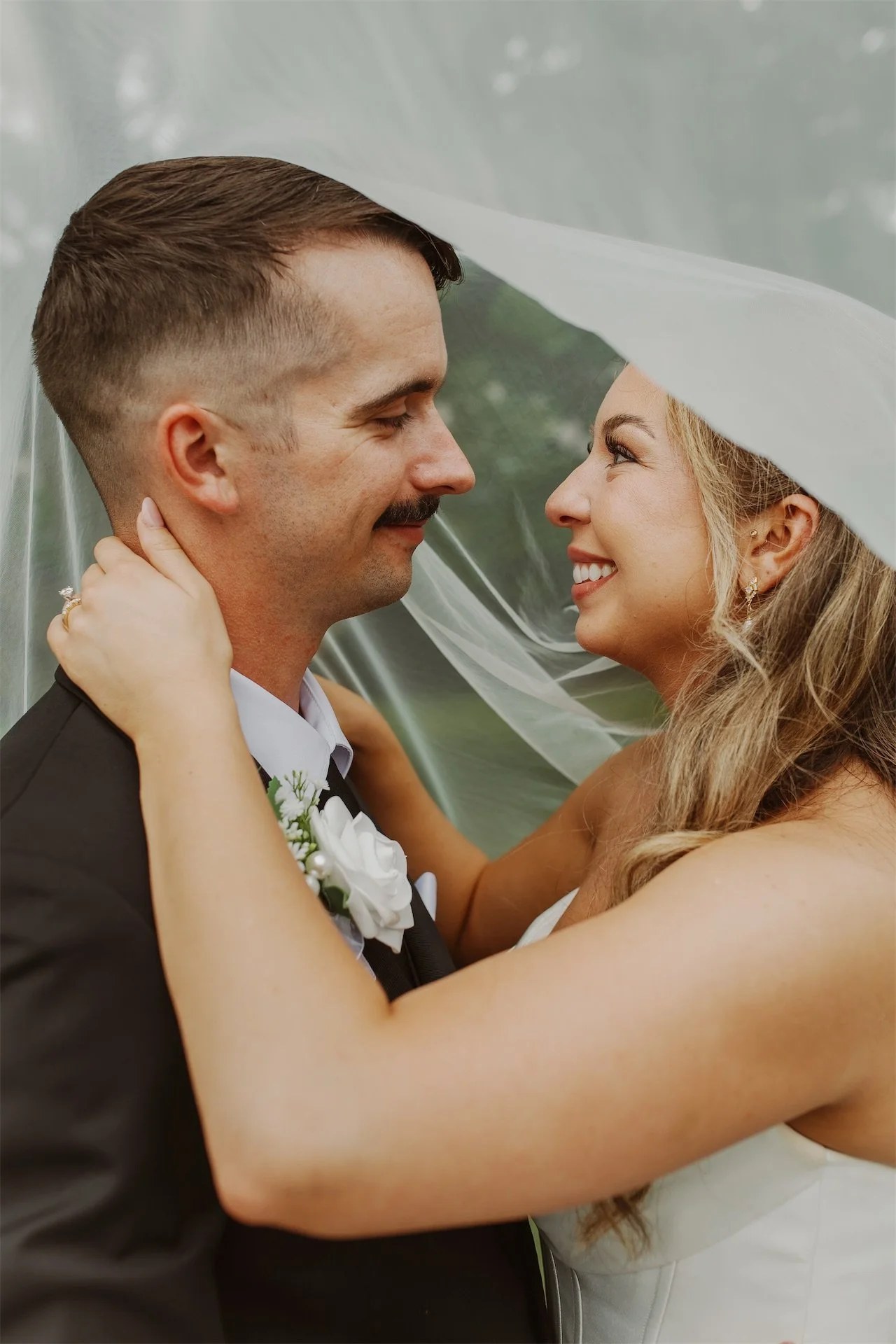 Bride and groom smiling nose to nose beneath flowing wedding veil