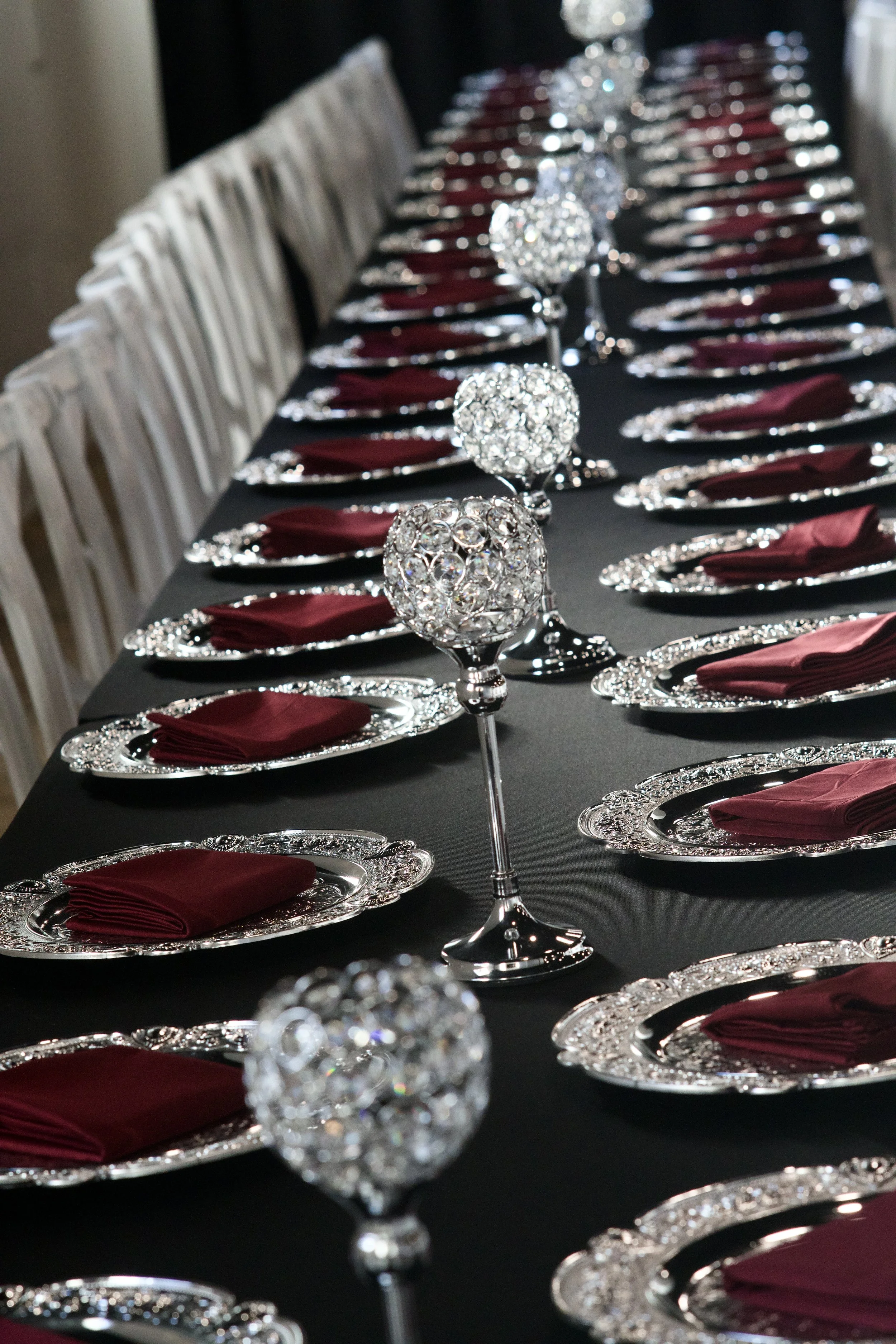 full reception table lined with crystal centerpieces and burgundy napkin settings