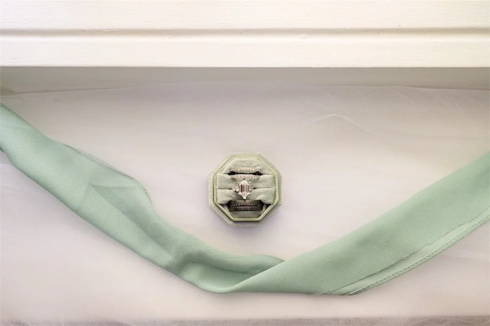 Octagon velvet ring box resting on a flowing sage green ribbon over a white veil