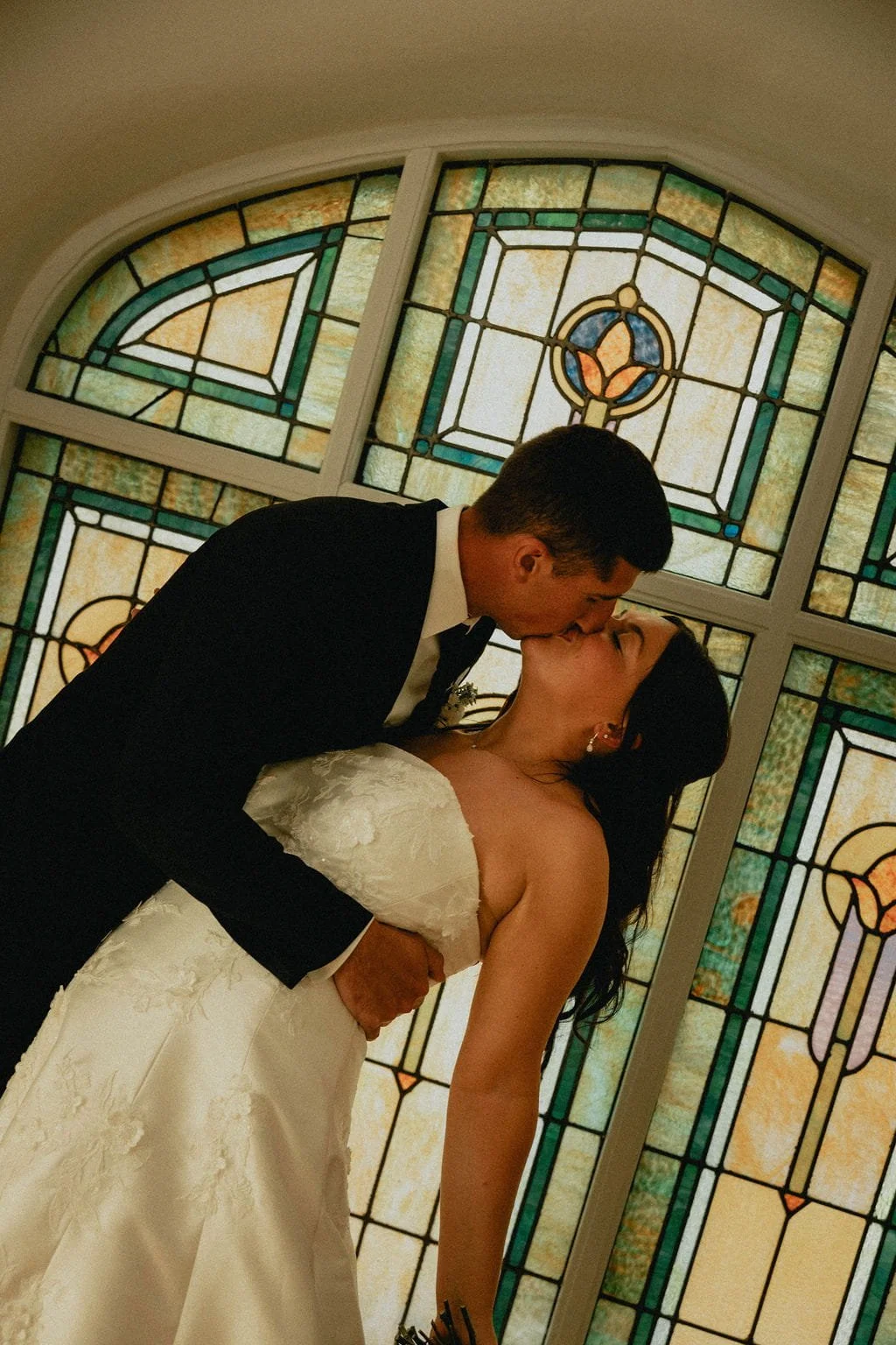 groom-kisses-bride-in-front-of-stained-glass-window.jpg