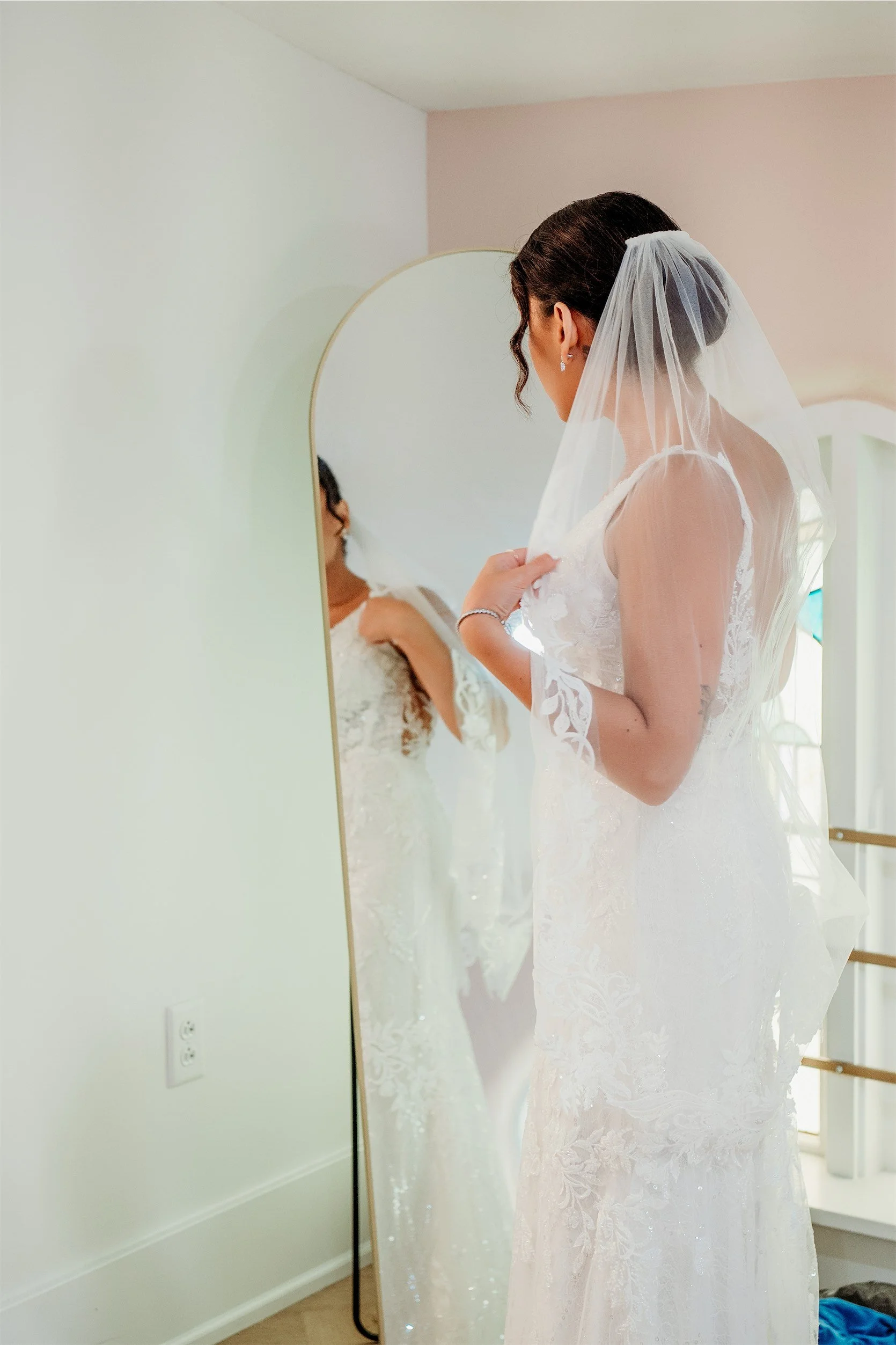 Bride checking her lace veil and wedding gown in a tall arched mirror inside the bridal suite