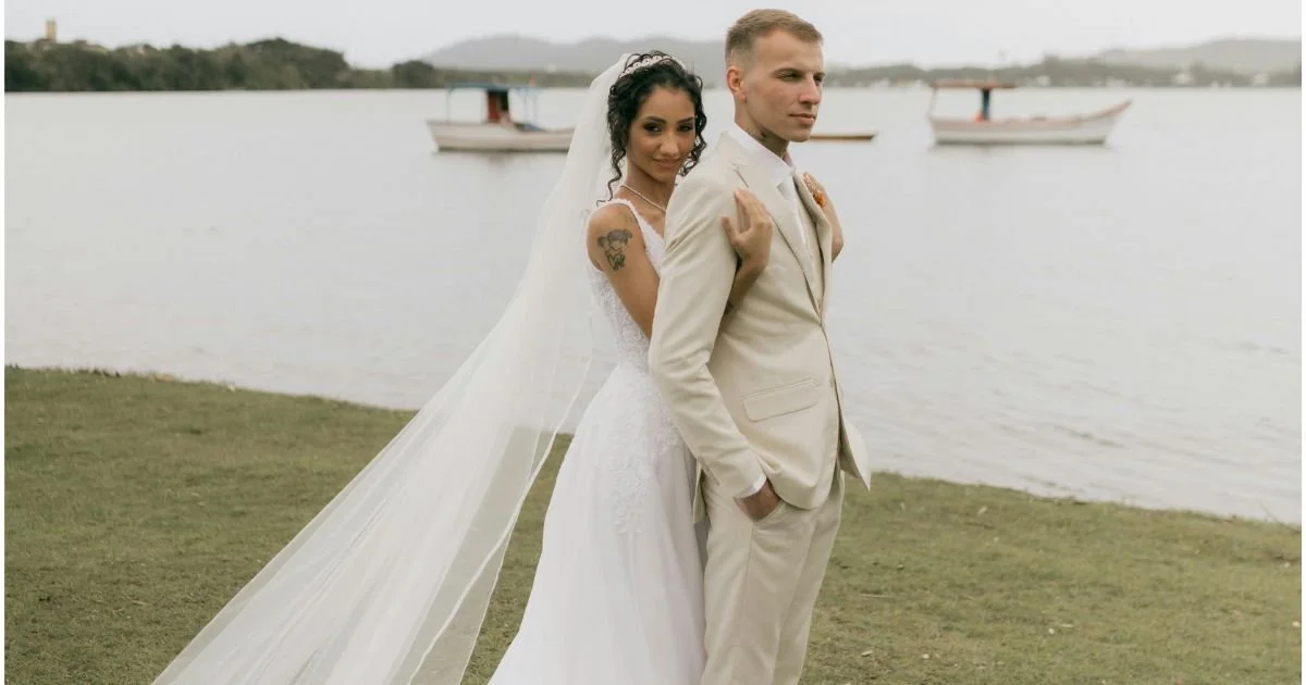 Bride and groom in cream suit pose back to back on a lakeside in Kosciusko County Indiana