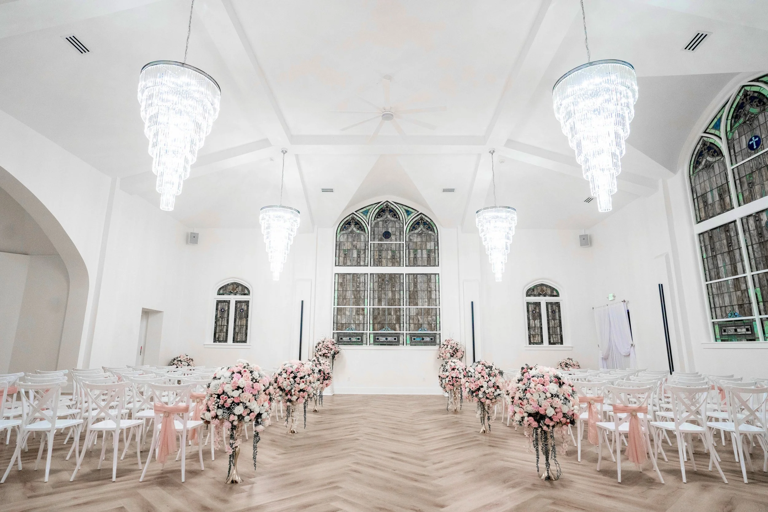 historic church ceremony space with stained glass windows, crystal chandeliers, pink floral arrangements
