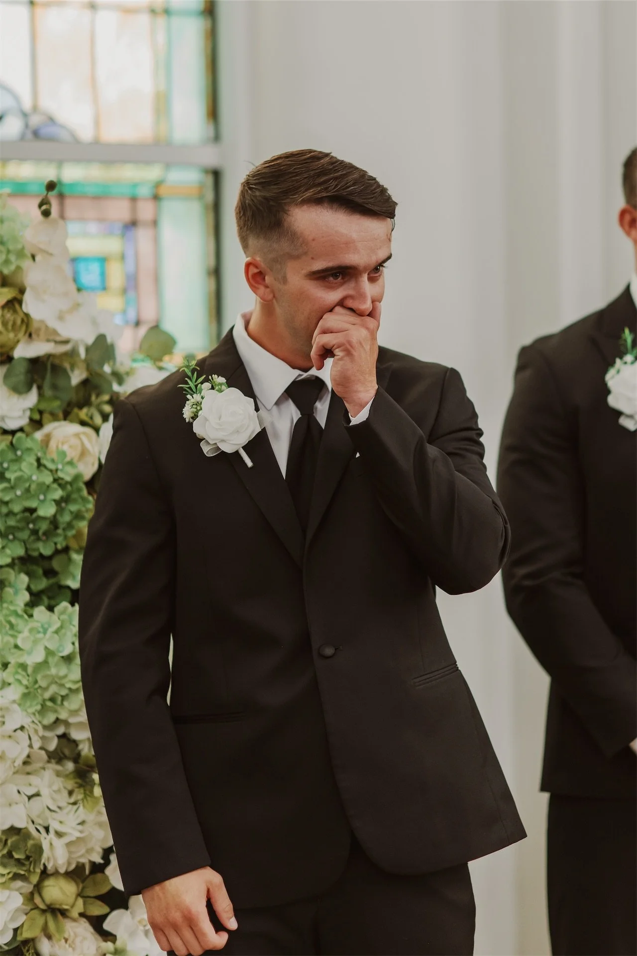 Groomsman wiping tears during emotional moment at church wedding ceremony