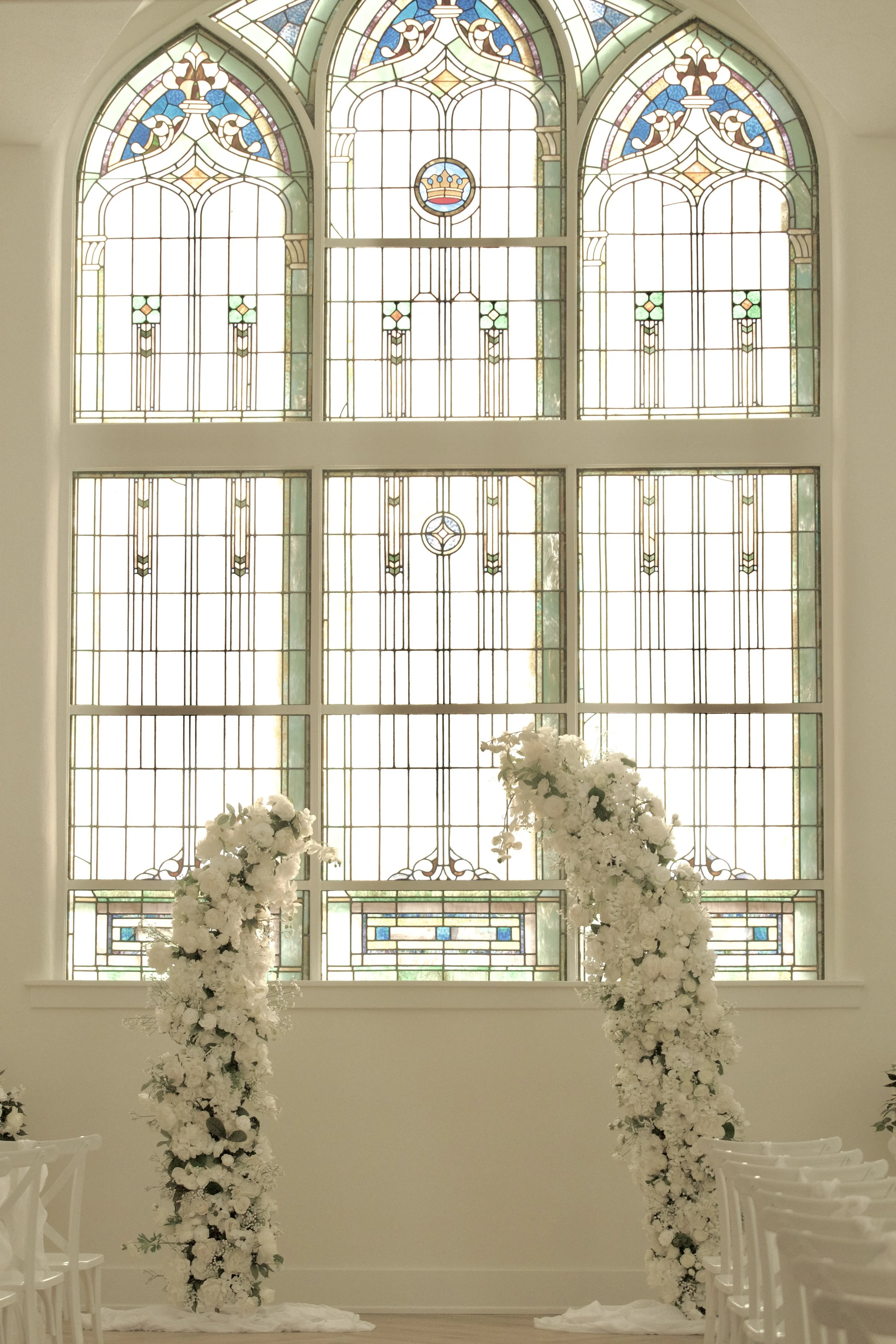 arched stained glass church window with cascading white floral installation below