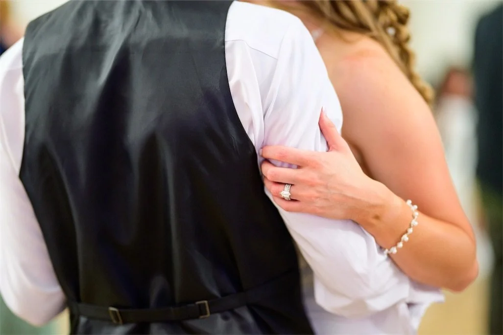 Close up of the bride's hand with a wedding ring on the groom's vest during a slow dance