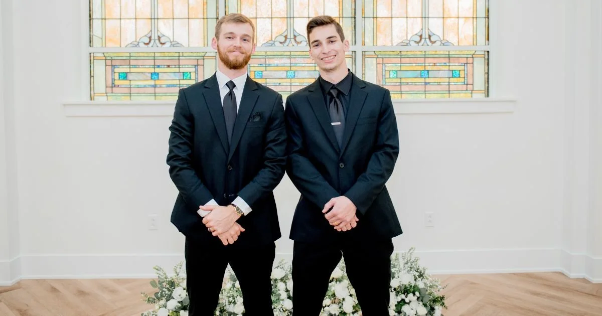 groomsmen in classic black tie attire standing before an arched stained glass window