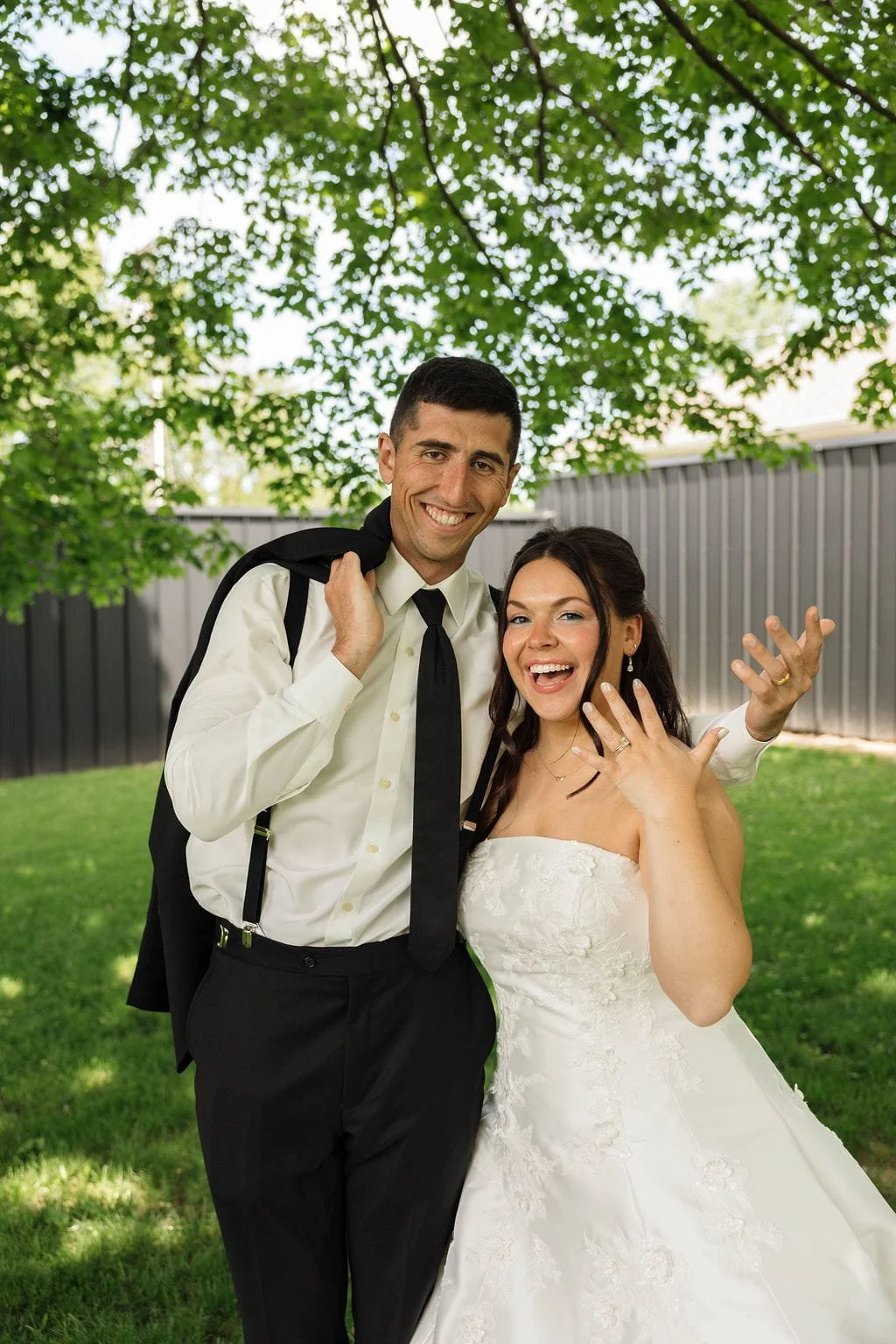 newlyweds-showing-wedding-rings-under-tree.jpg