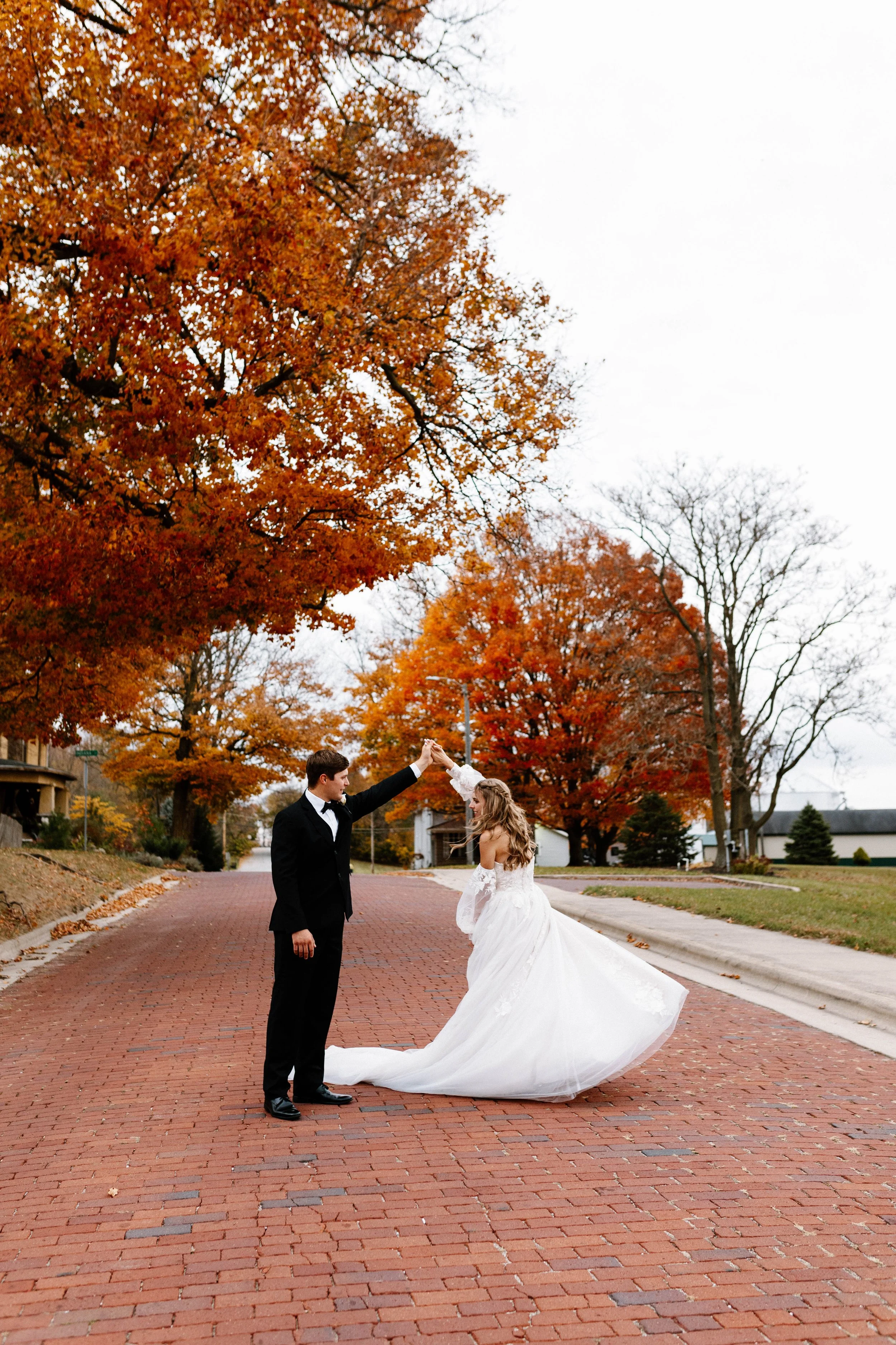 A bride and groom dancing on a brick street surrounded by fall foliage.