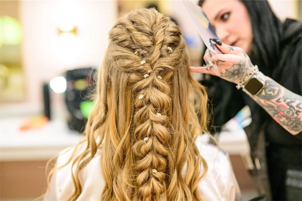 Hair stylist finishing a bride's long half up braid decorated with small pearl pins