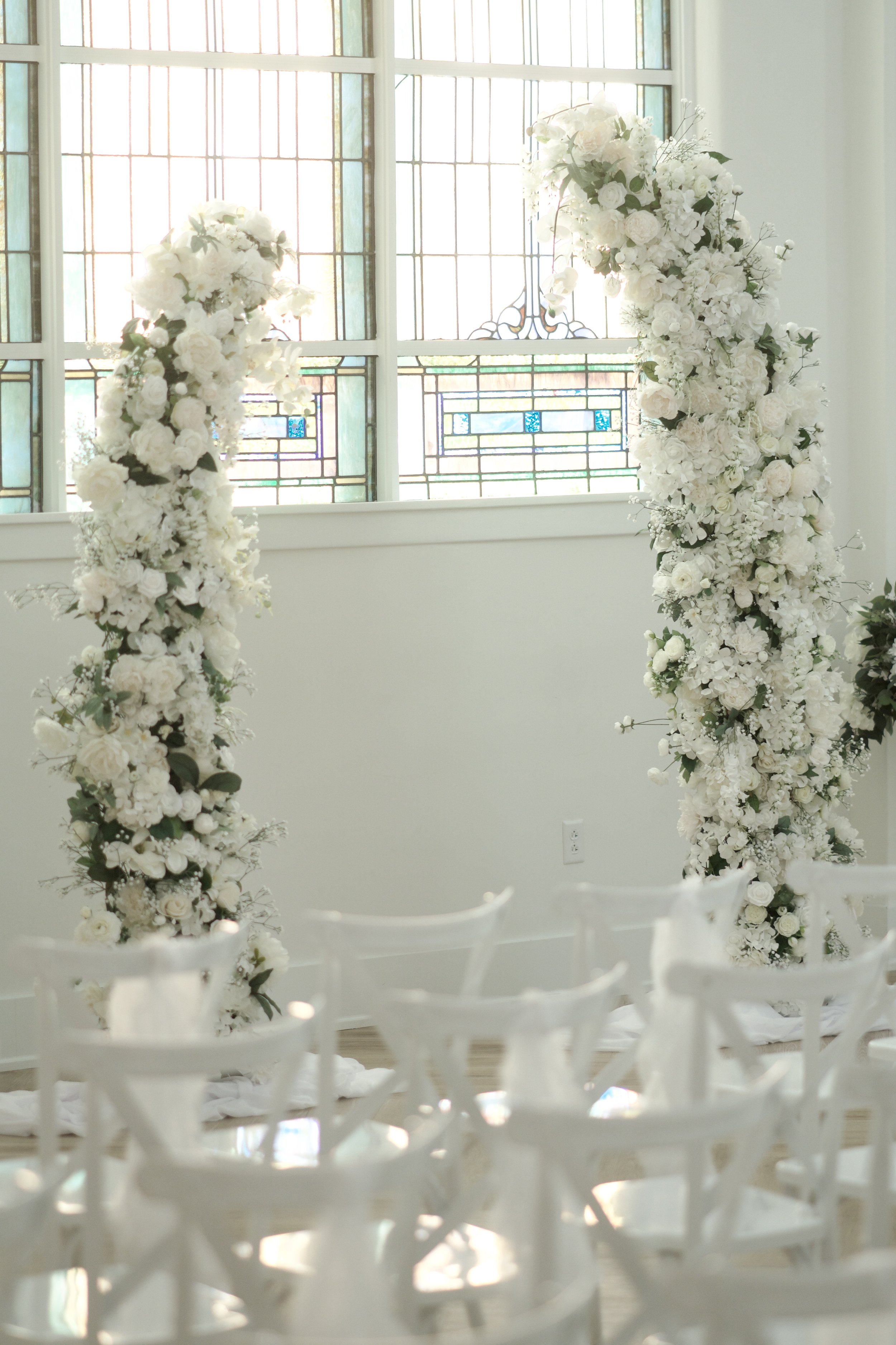 white floral columns rising beneath stained glass windows at a Gatsby ceremony