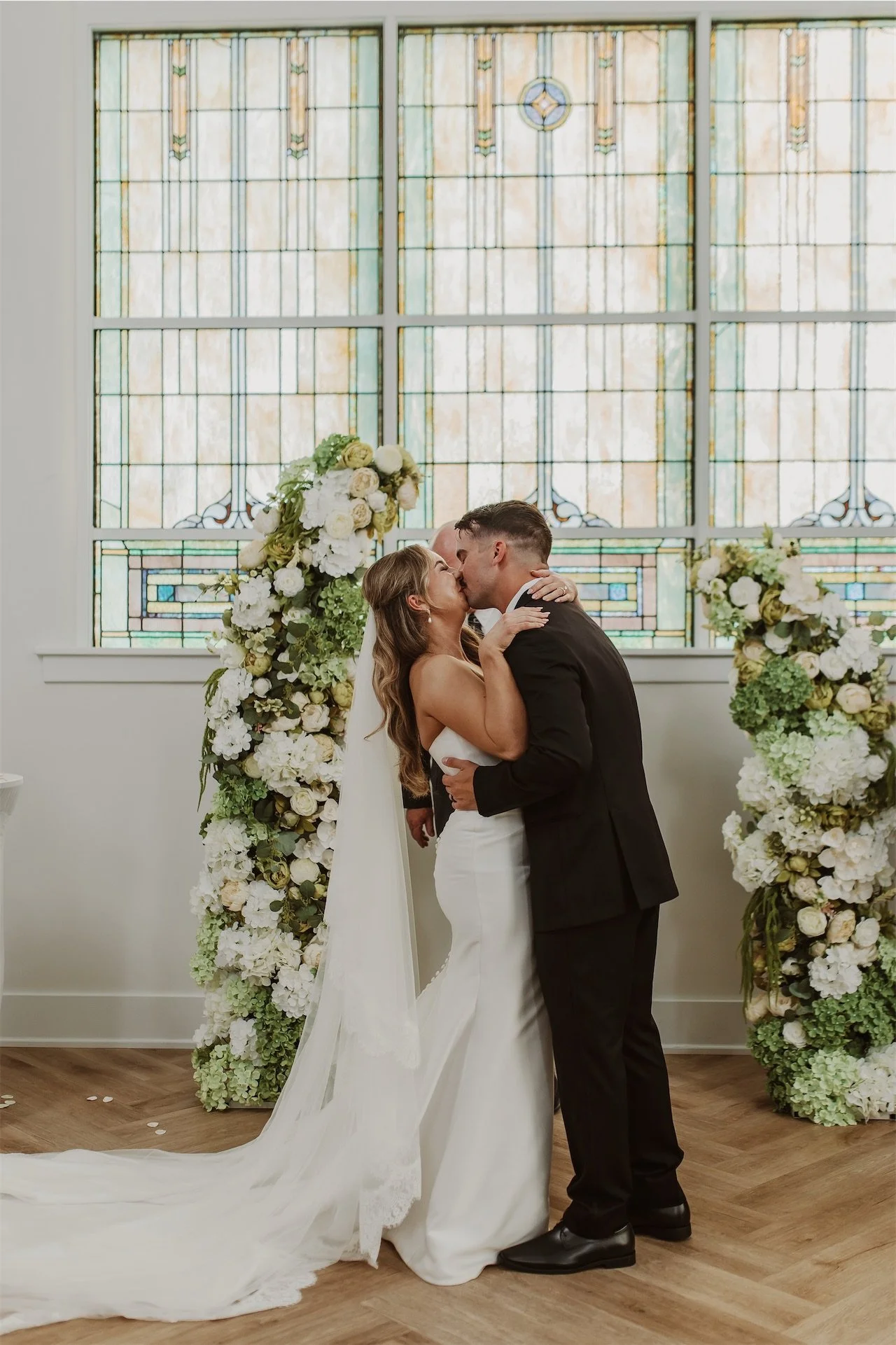 Bride and groom sharing first kiss as married couple before stained glass altar