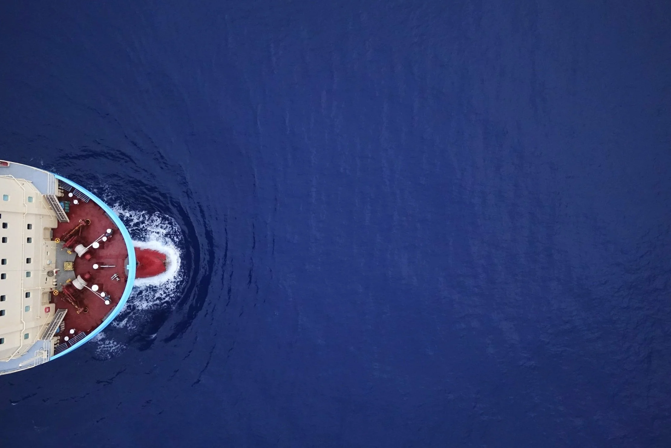 An aerial shot looking straight down at the blue ocean with the bow of a large ship visible at the edge of the photo.
