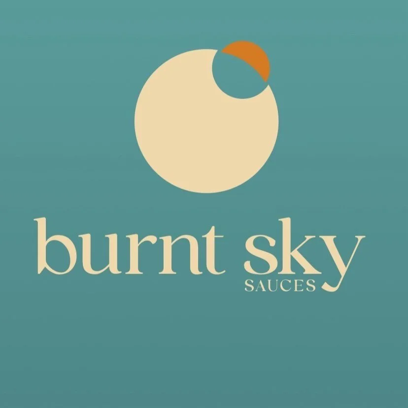 Logo for Burnt Sky Sauces featuring a stylized circle with a smaller semi-circle on top, resembling a planet or sun, on a teal background with the brand name in beige text.