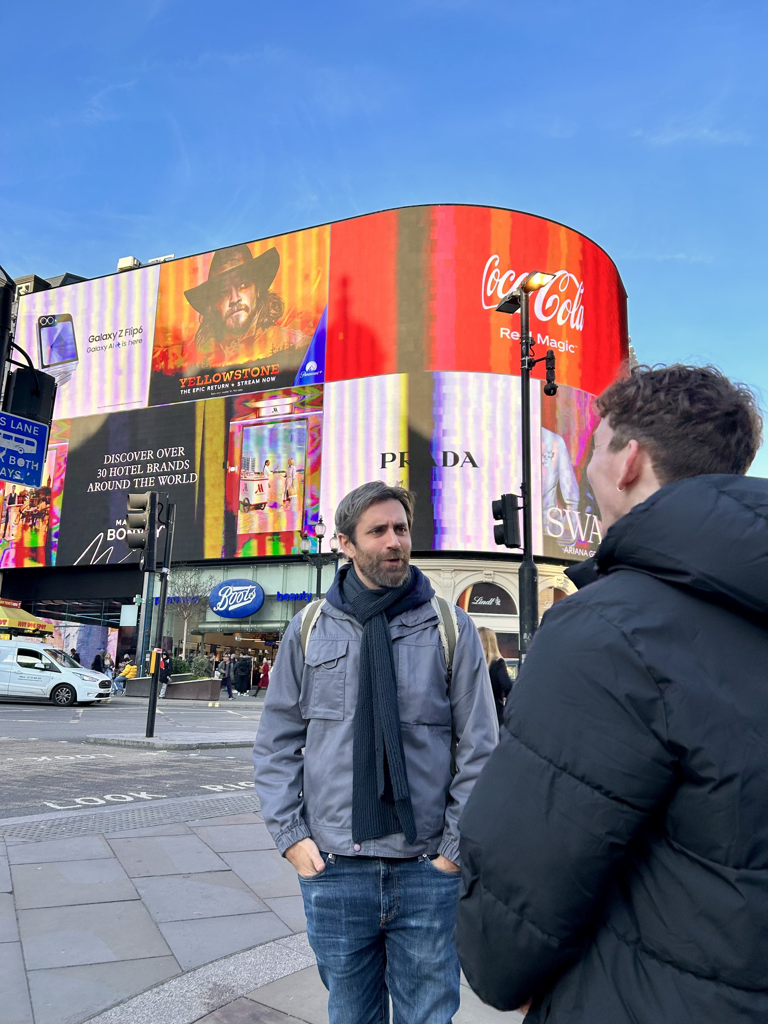 A tour guide and a man talking in front of the famous Piccadilly Circus billboards on a movie locations tour.