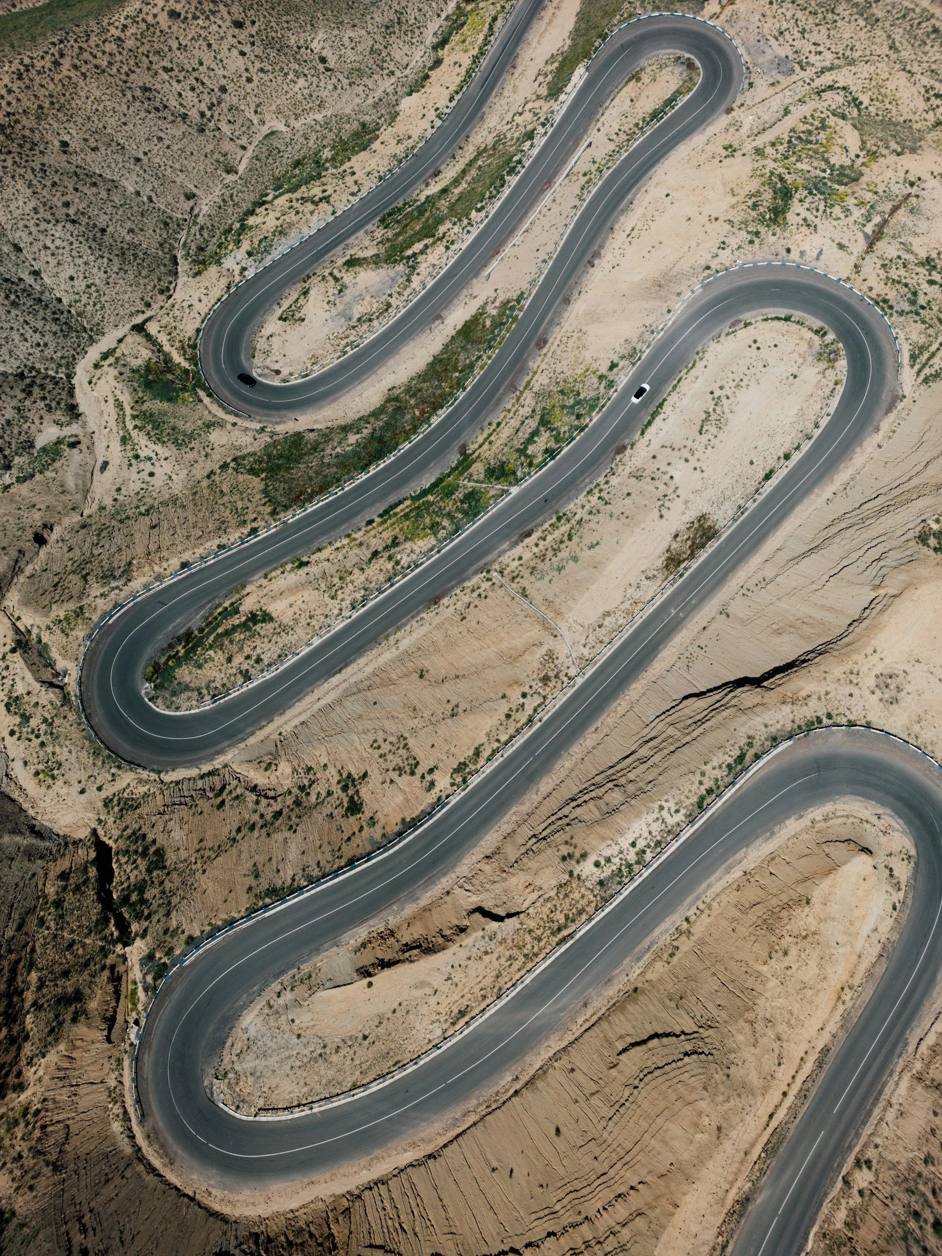 Aerial view of a winding mountain road with sharp curves, surrounded by dry, rugged landscape.