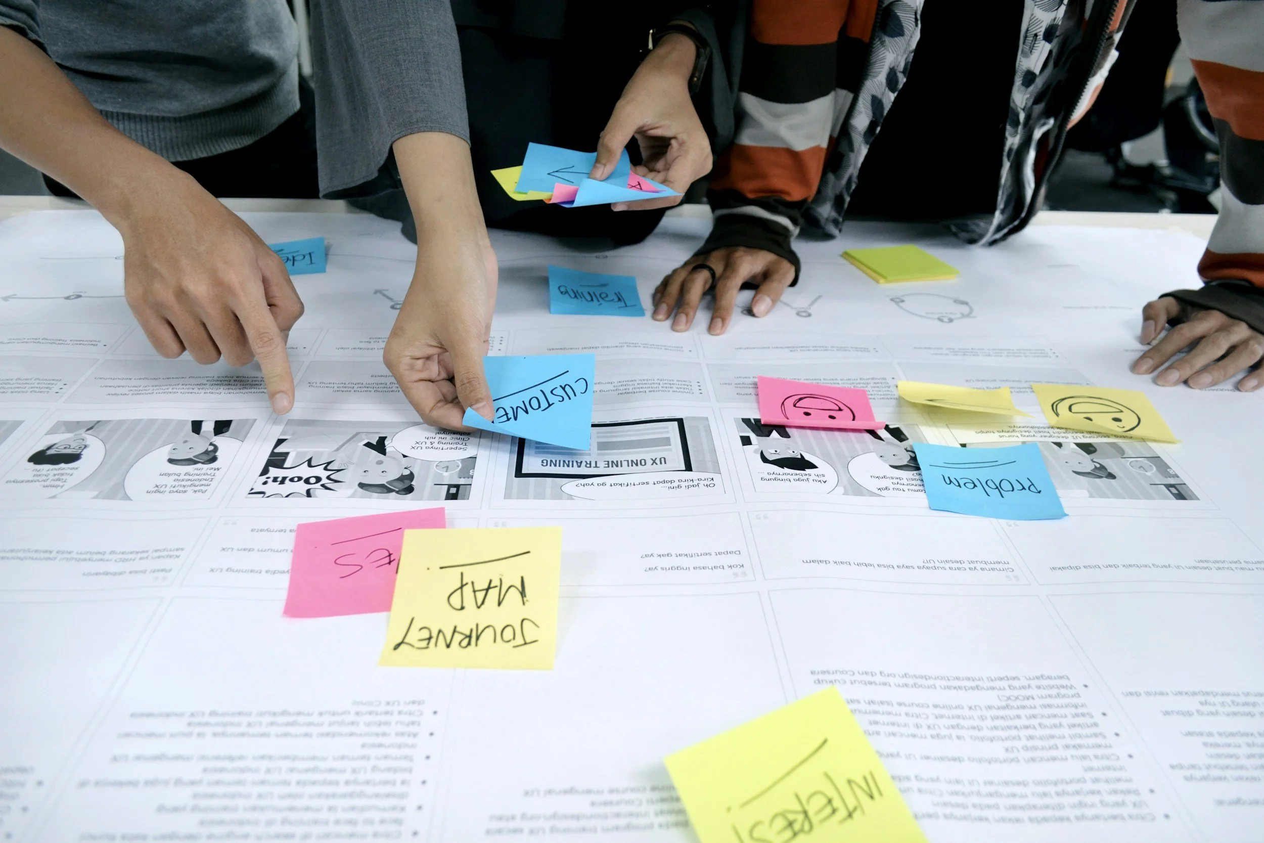 People collaborating around a table with printed documents and colorful sticky notes, actively discussing and pointing to ideas for a project.